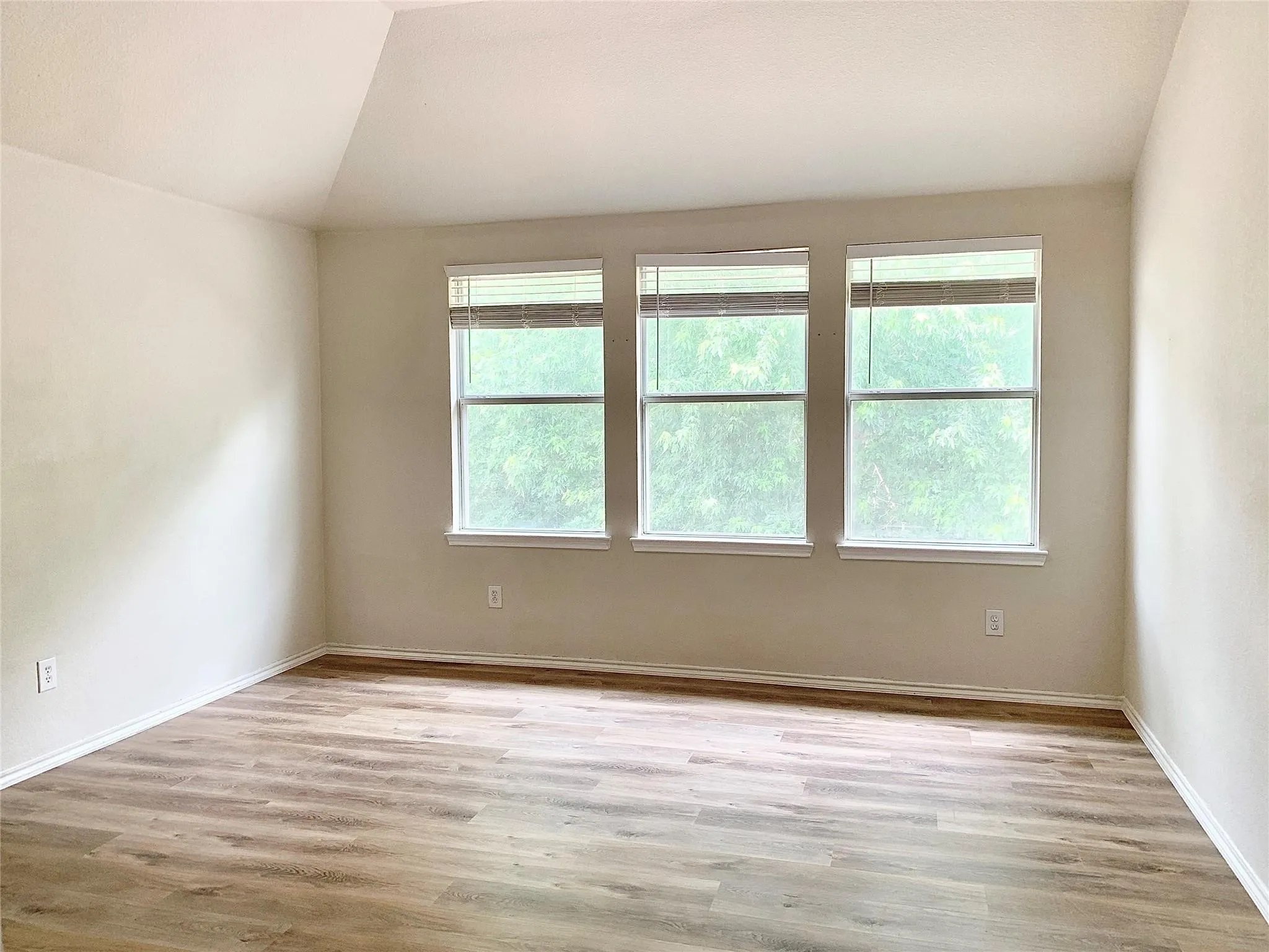Sloped ceiling with recessed lighting, three windows, wood-finish flooring, and neutral wall tones