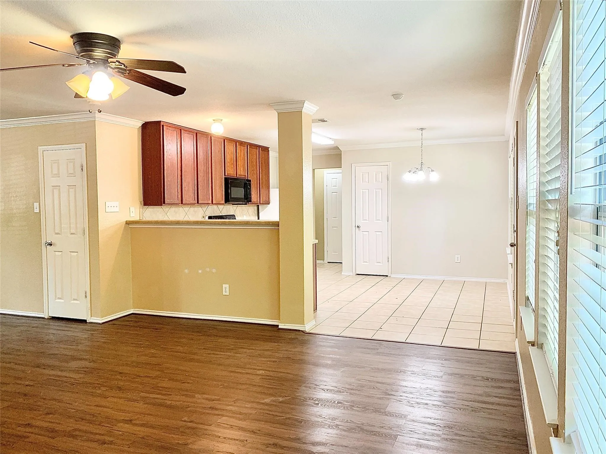 Wood-finish flooring, ceiling fan with light fixture, white interior doors, kitchen with wood cabinetry and built-in microwave, tile flooring