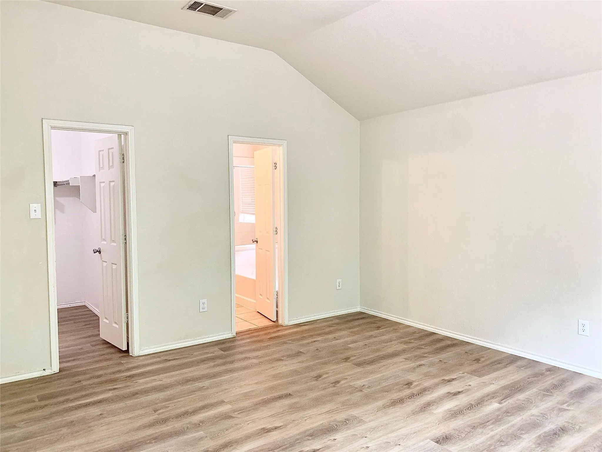 Vaulted ceiling, wood-finish flooring, and white walls