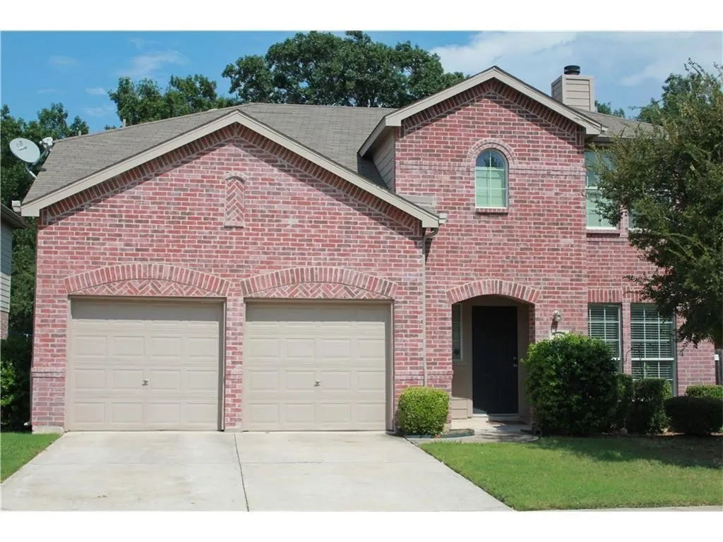 Red brick exterior with arched brickwork accents, two-car garage, covered entry, and mature landscaping