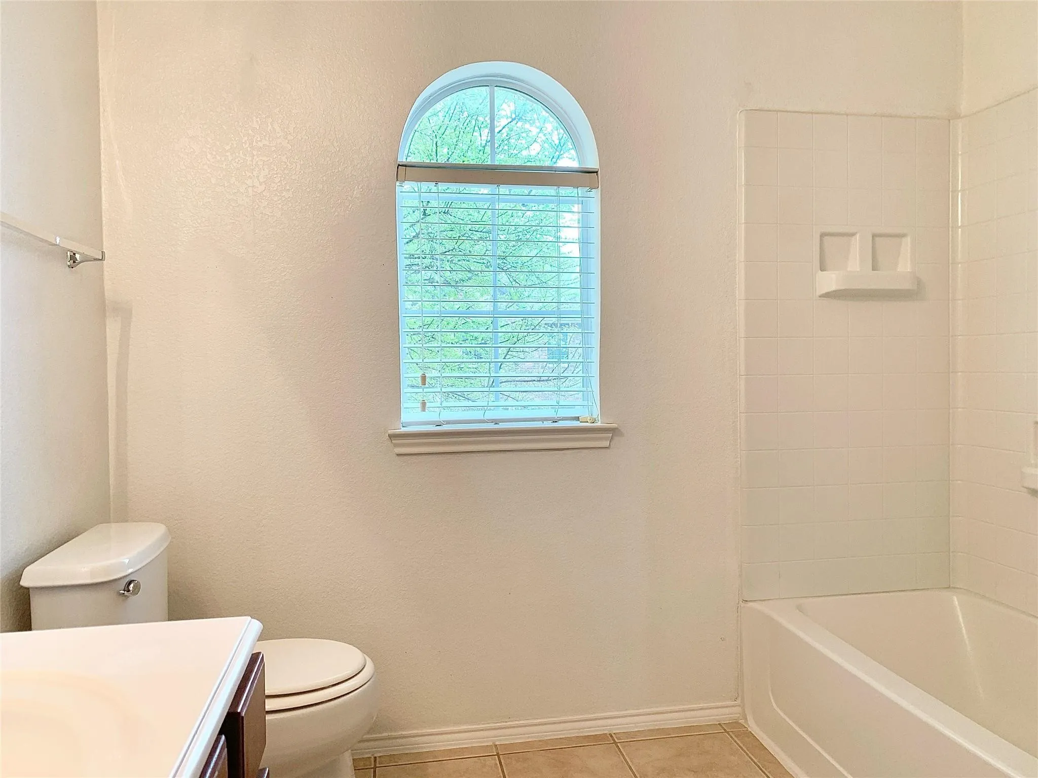 Arched window, ceramic tile flooring, built-in bathtub, and a tiled shower surround