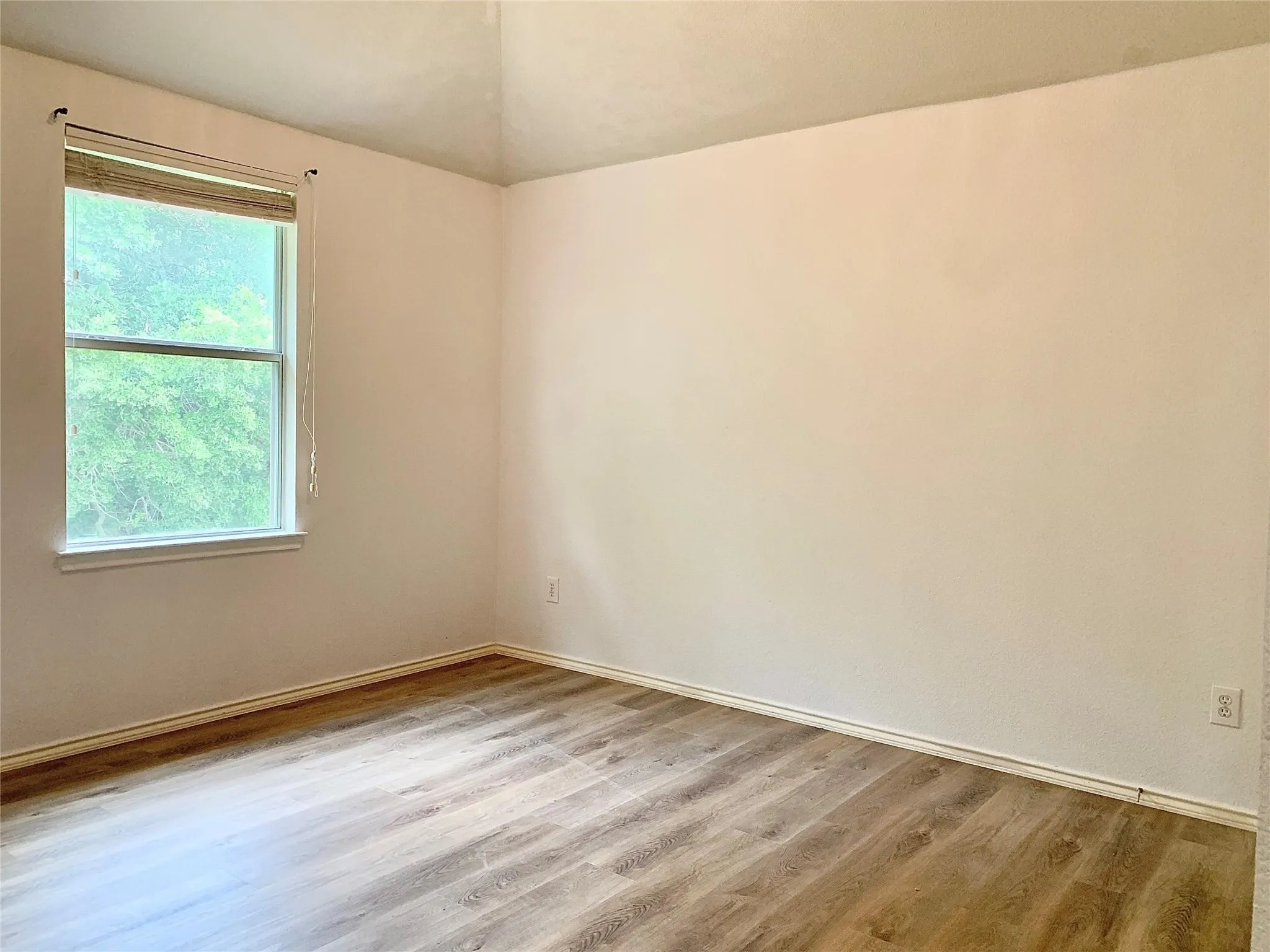 Wood-finish flooring with baseboard trim, neutral wall tones, and a window with blinds
