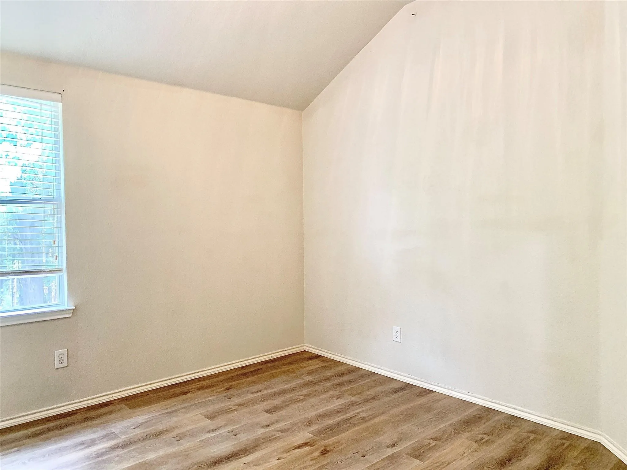 Vaulted ceiling, wood-finish flooring, and window with blinds