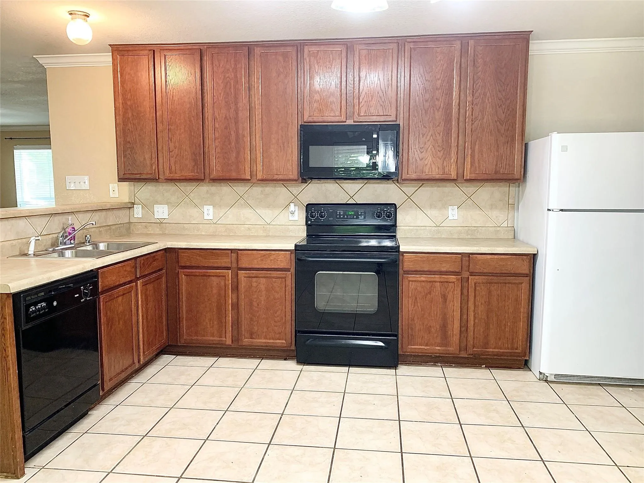 Wood-finish cabinetry, tile backsplash, built-in microwave, integrated dishwasher, and tile flooring
