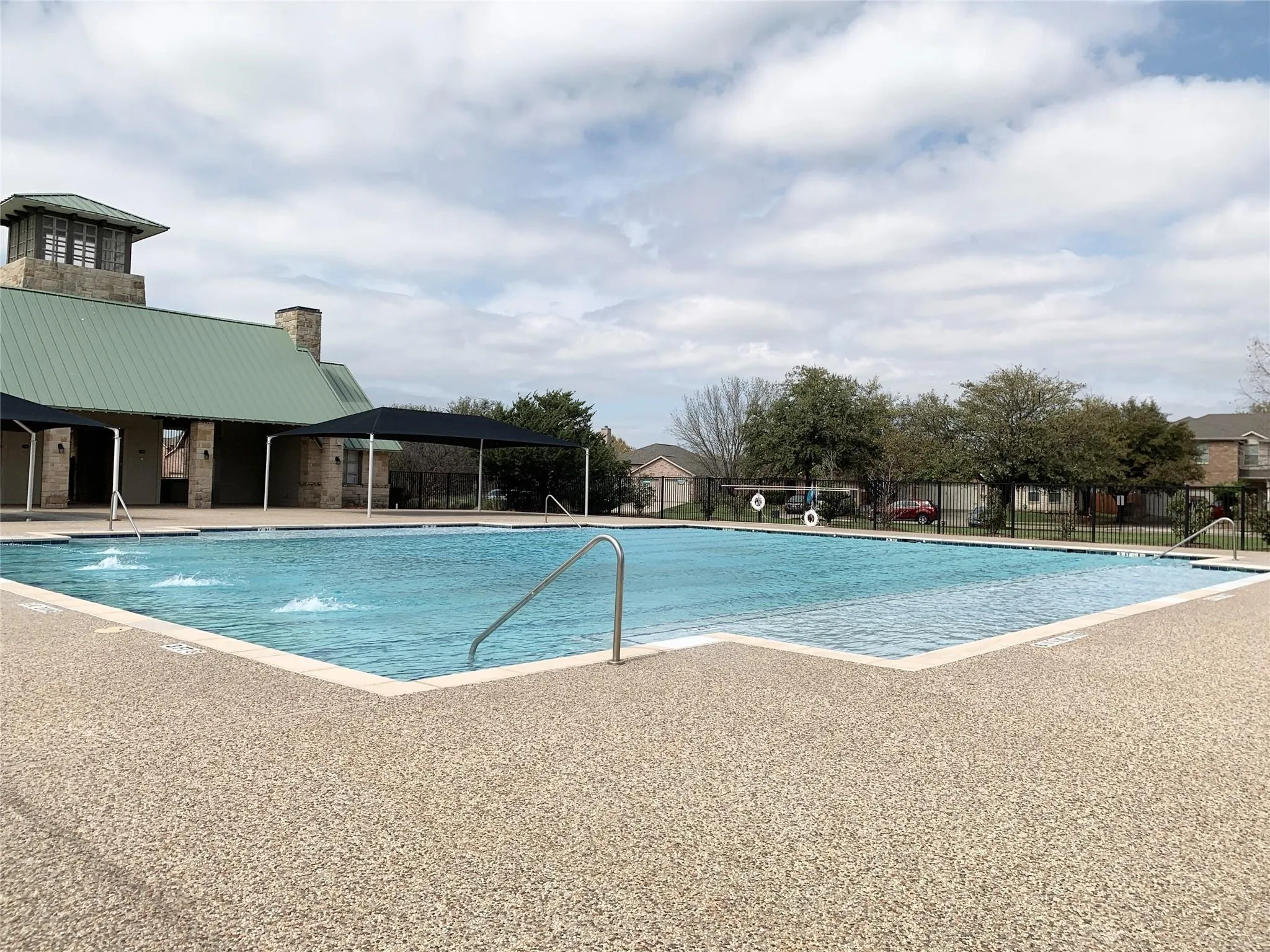 Expansive swimming pool with a textured concrete deck, featuring multiple water jets and stainless steel handrails