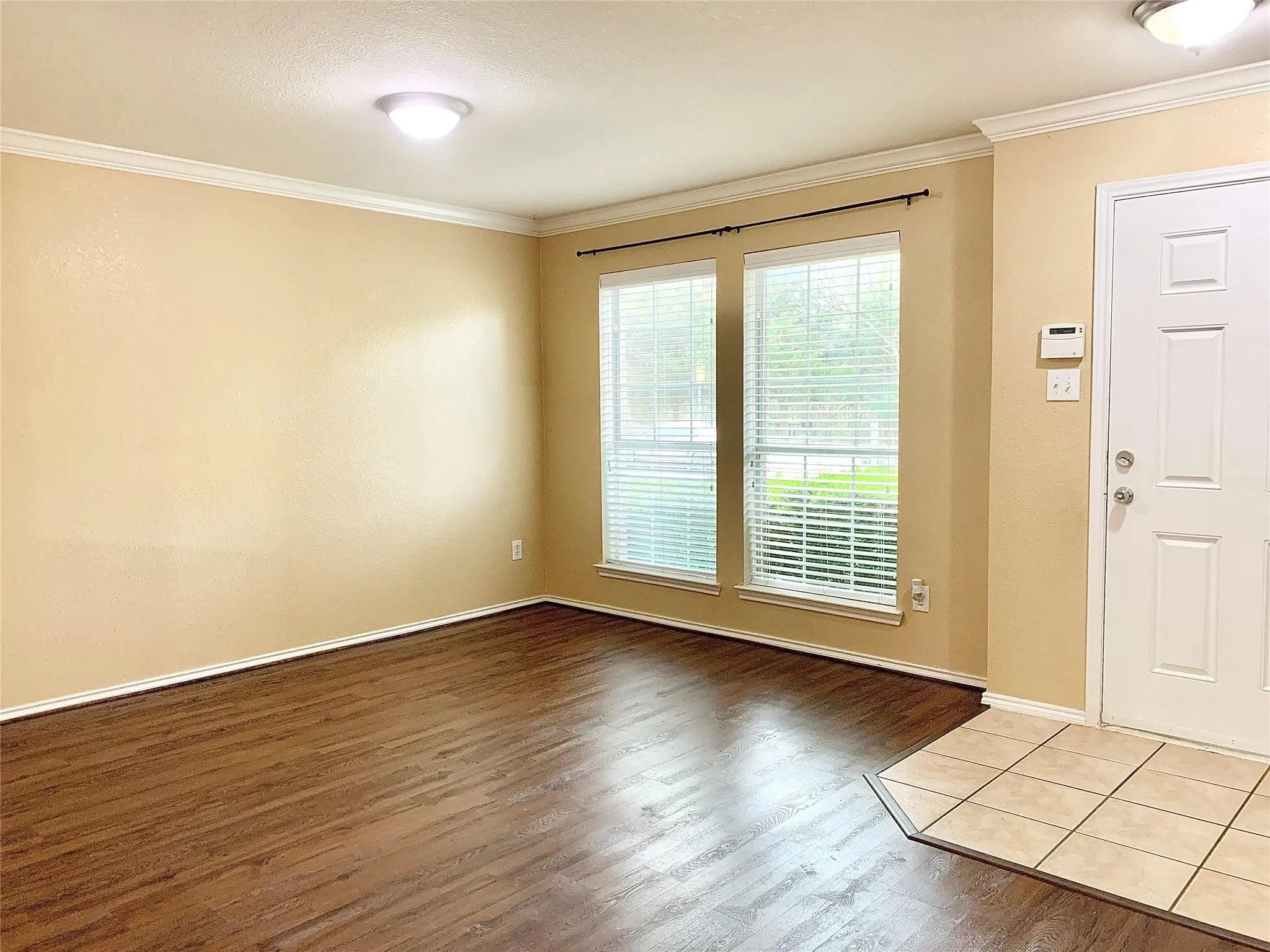 Wood-finish flooring with a tile entry, two windows, and crown molding