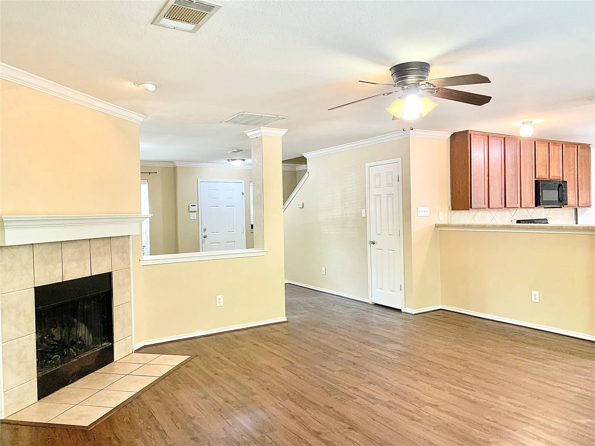 Wood-finish flooring throughout, tile-surround fireplace with hearth, built-in microwave, wood cabinetry, and a ceiling fan with integrated lighting