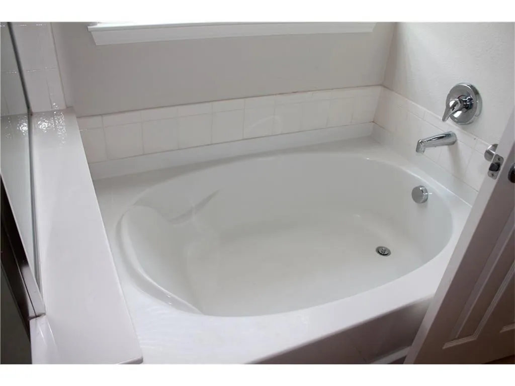 Recessed soaking tub with chrome fixtures and white tiled surround