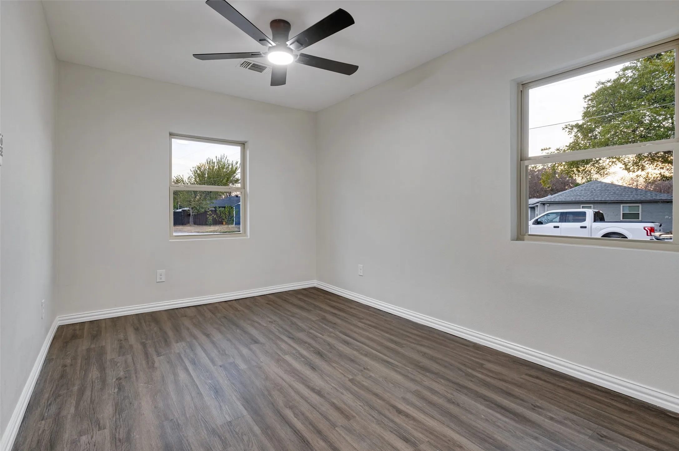 Neutral wall color, wood-finish flooring, two windows, and a ceiling fan with integrated lighting