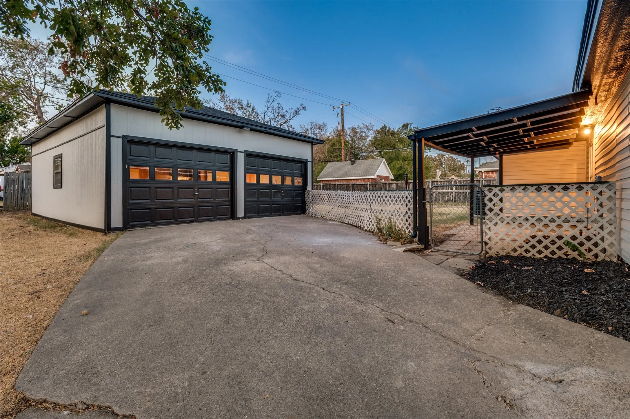 Detached two-car garage with black paneled doors, covered patio structure, and concrete driveway