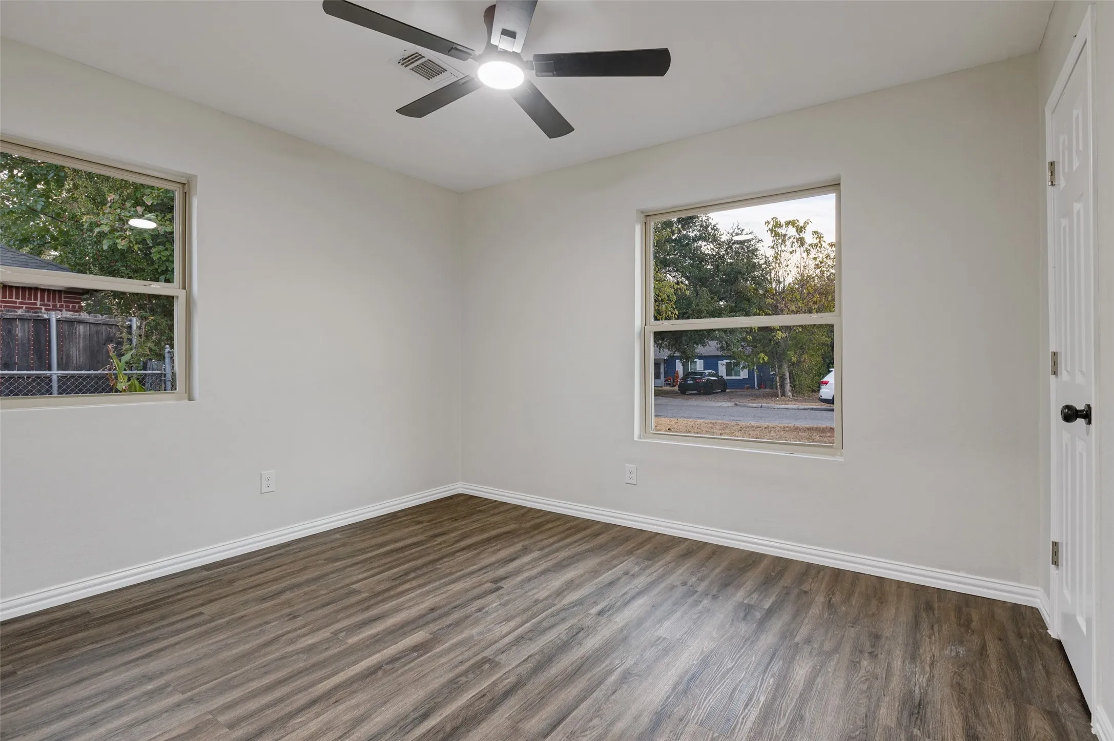 Neutral wall finishes, wood-finish flooring, two large windows, white trim, and a ceiling fan with integrated lighting