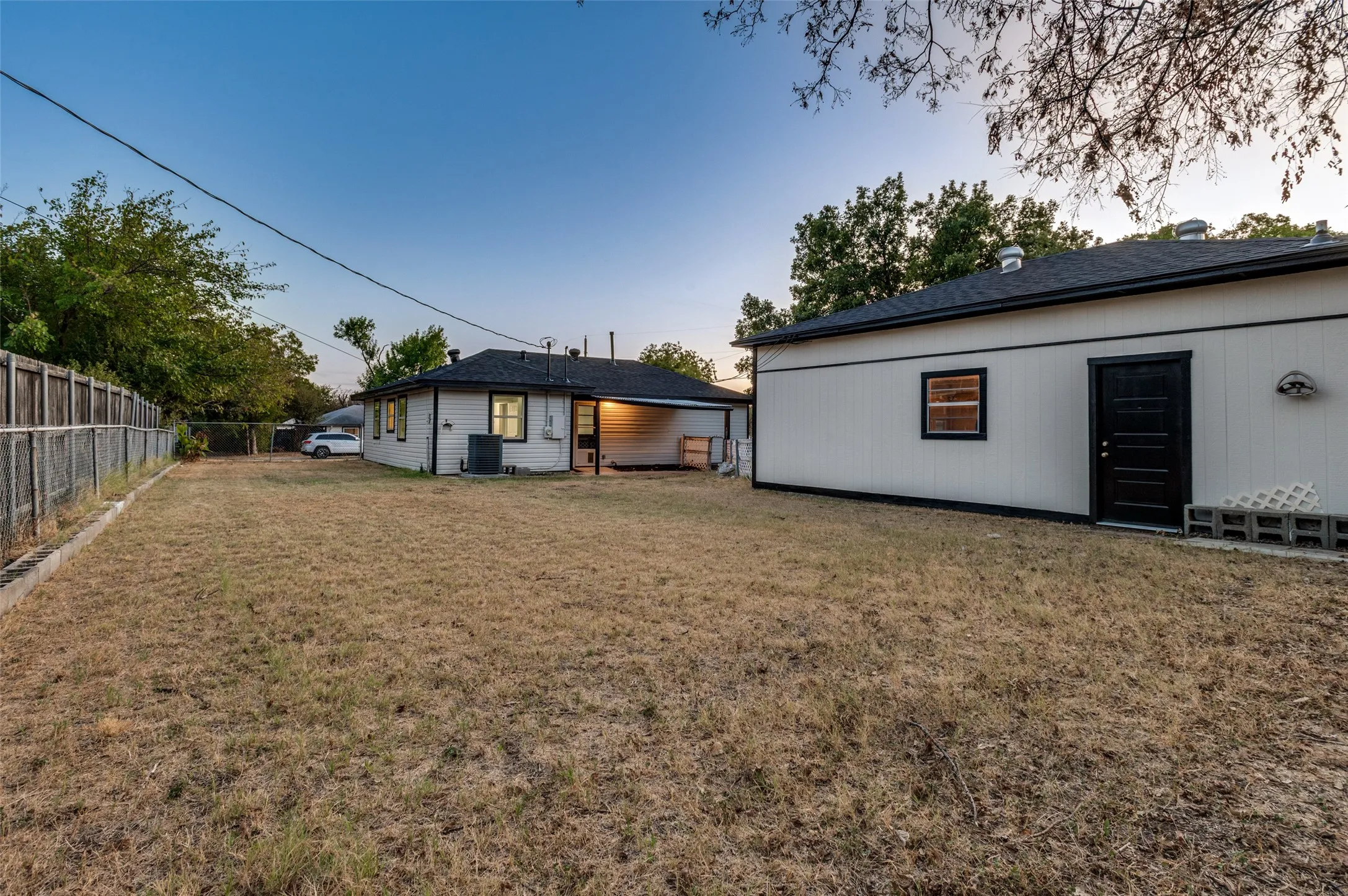 Expansive backyard featuring a privacy fence, an auxiliary building with a dark-paneled door, and a covered patio area
