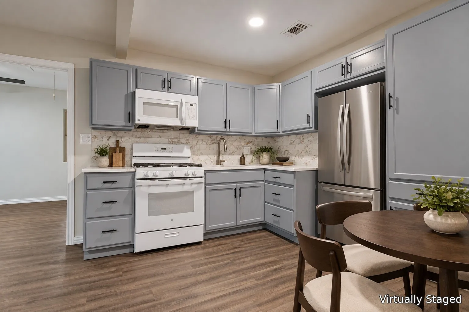 Kitchen featuring wood-finish flooring, light gray cabinetry with black hardware, white countertops with a patterned backsplash, and stainless steel appliances