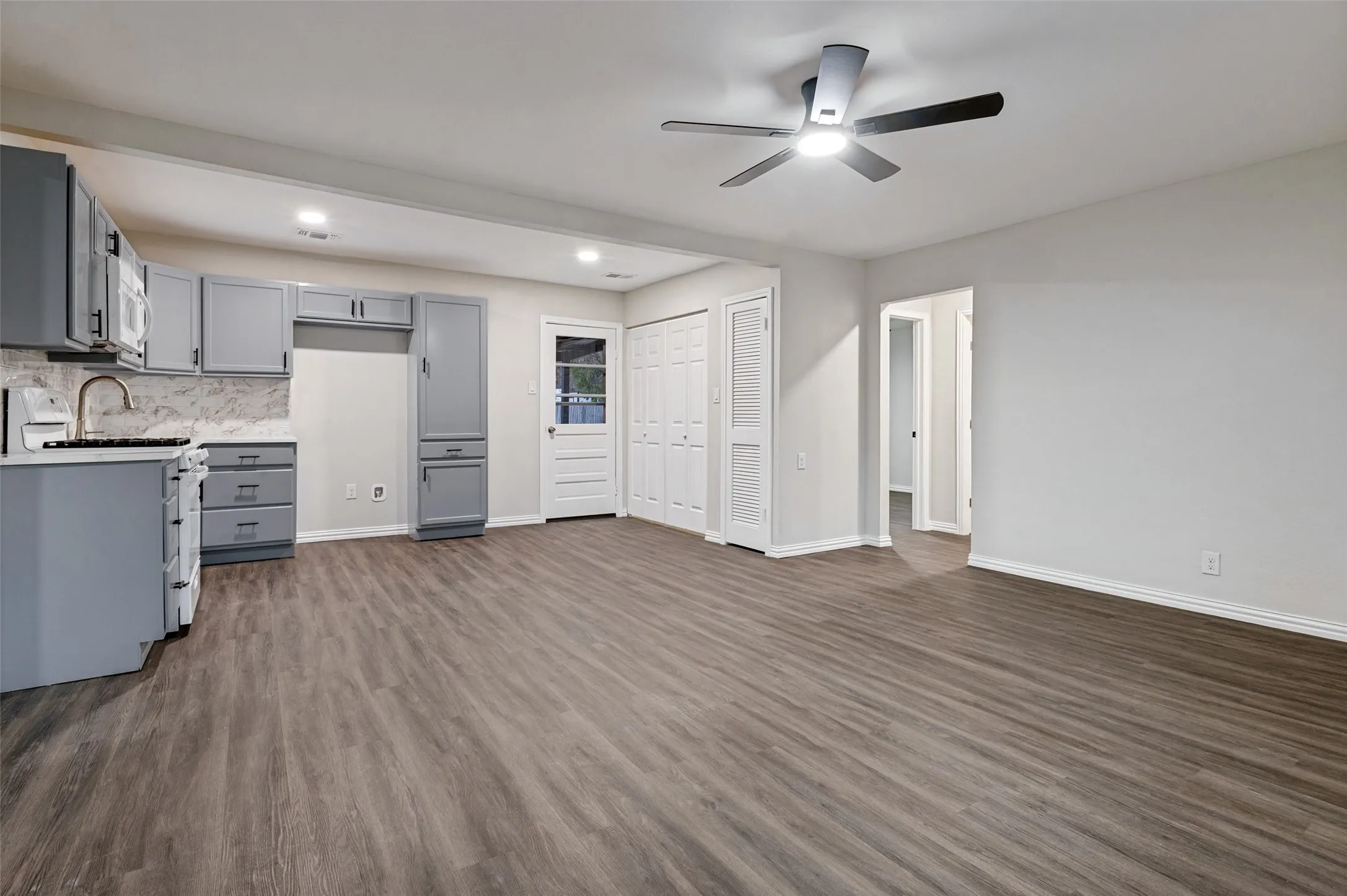 Open-concept living space featuring wood-finish flooring, a contemporary ceiling fan with integrated lighting, and gray cabinetry with modern hardware
