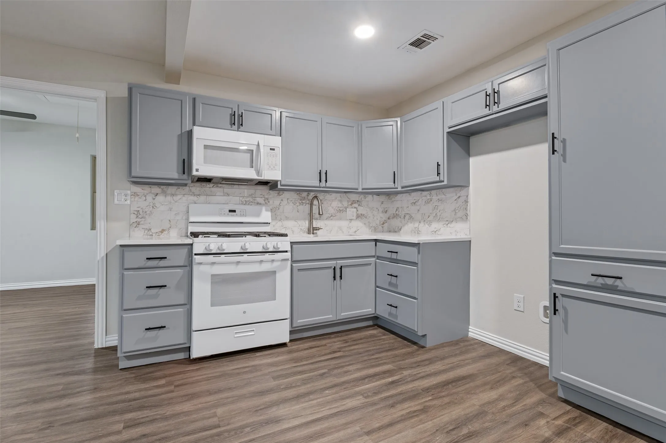 Kitchen featuring wood-finish flooring, light gray cabinetry, white countertops, and a white gas range with an over-the-range microwave