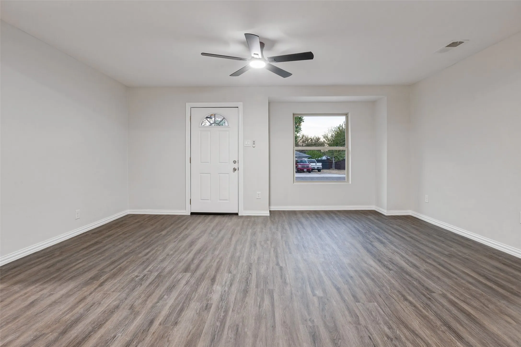 Recessed window, wood-finish flooring, ceiling fan with integrated lighting, paneled entry door with frosted glass insert, and light-toned wall finishes