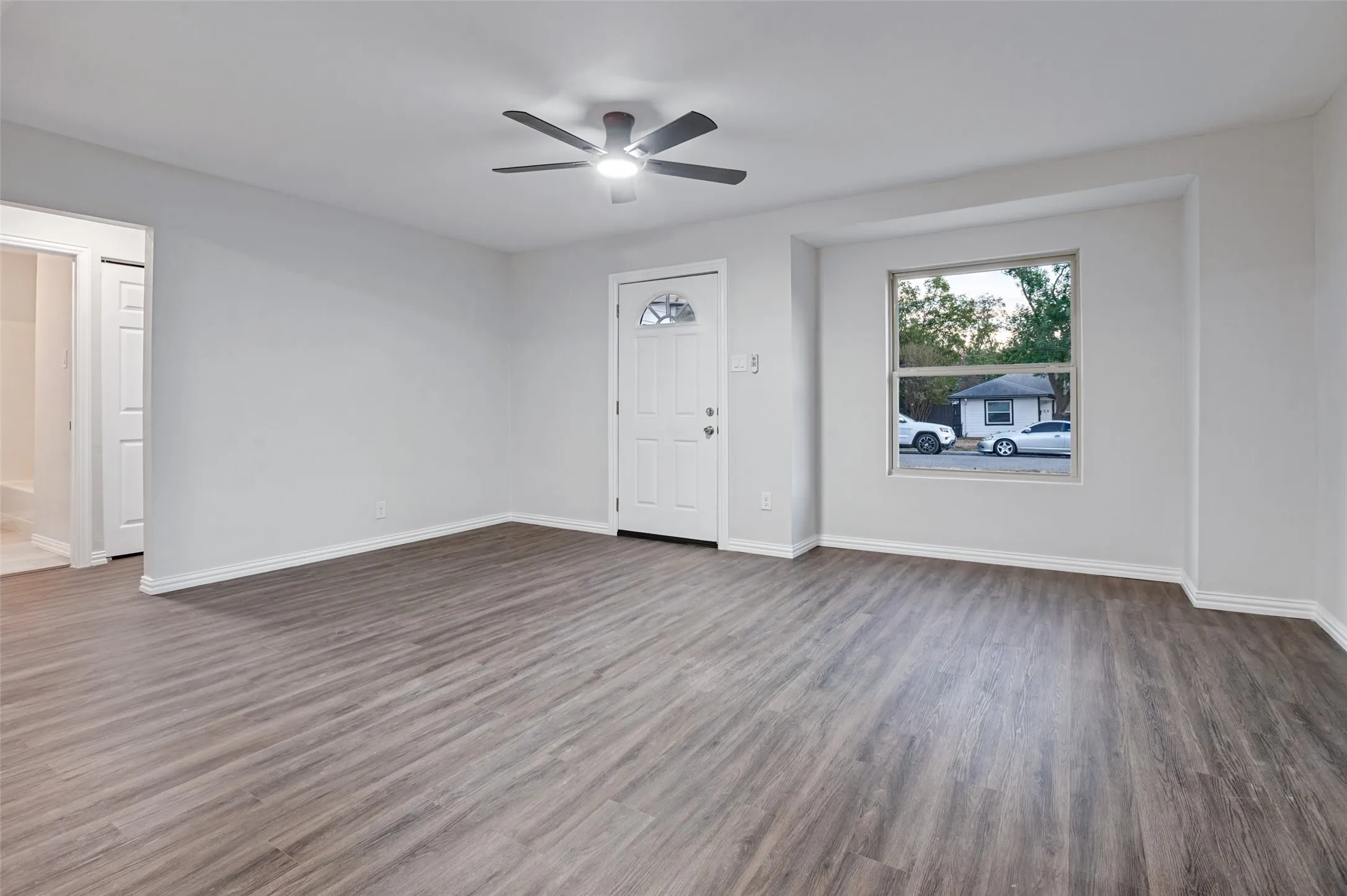 Spacious room with wood-finish flooring, a ceiling fan with integrated lighting, and neutral wall tones