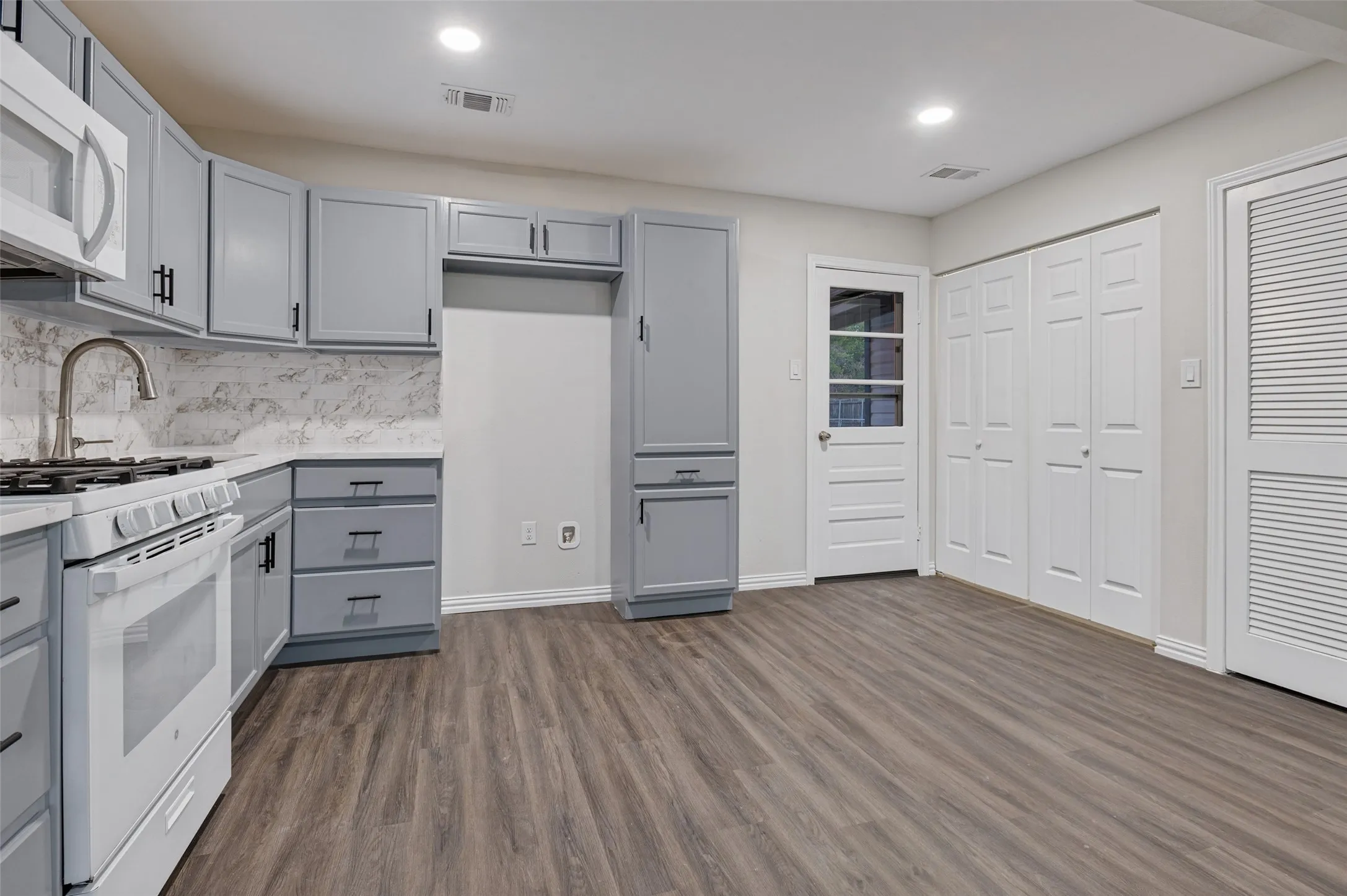 Kitchen featuring gray cabinetry with black hardware, white countertop surfaces, white subway tile backsplash, and wood-finish flooring