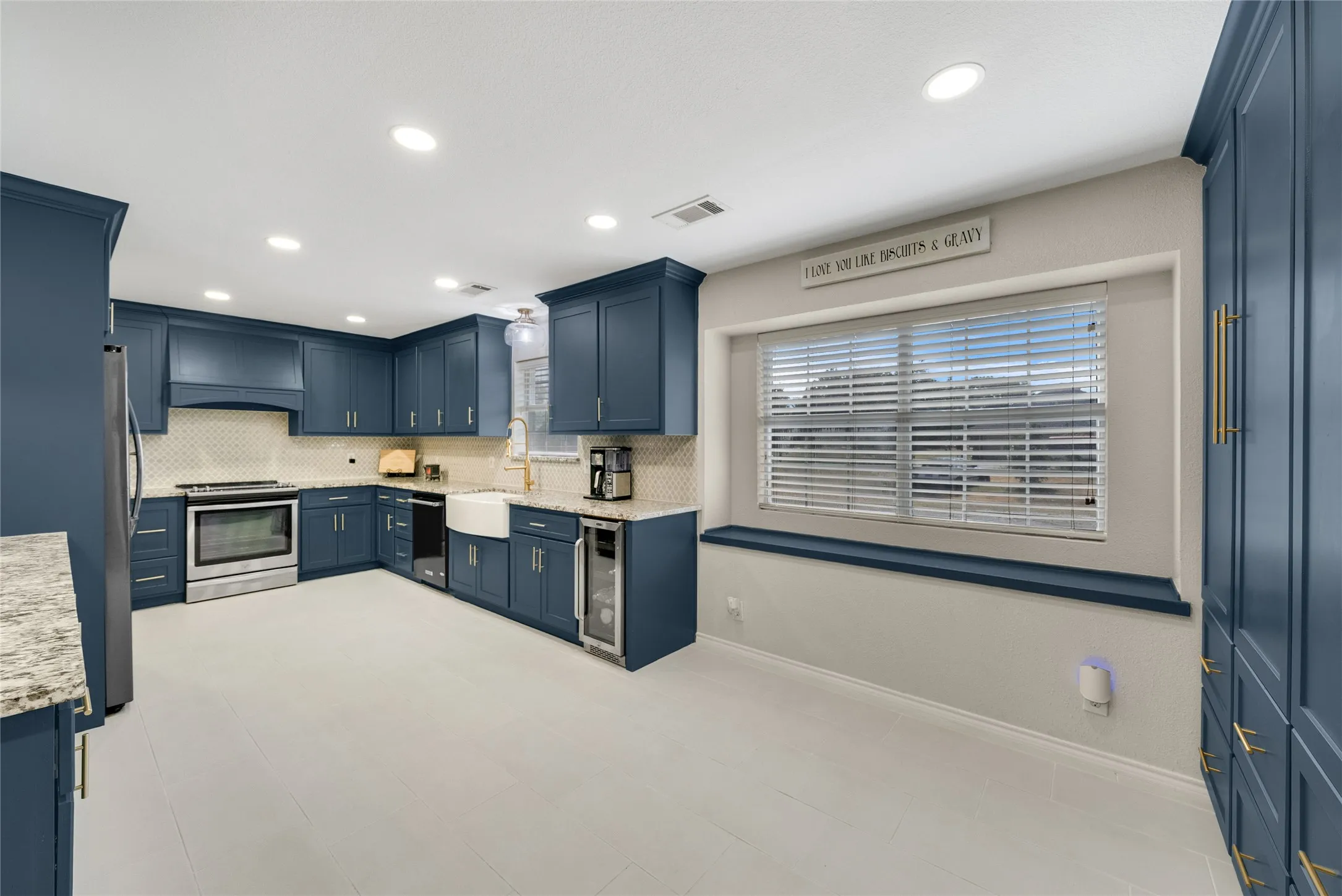 Kitchen featuring blue cabinetry, stainless steel appliances, a white farmhouse sink, light-toned flooring, and recessed lighting