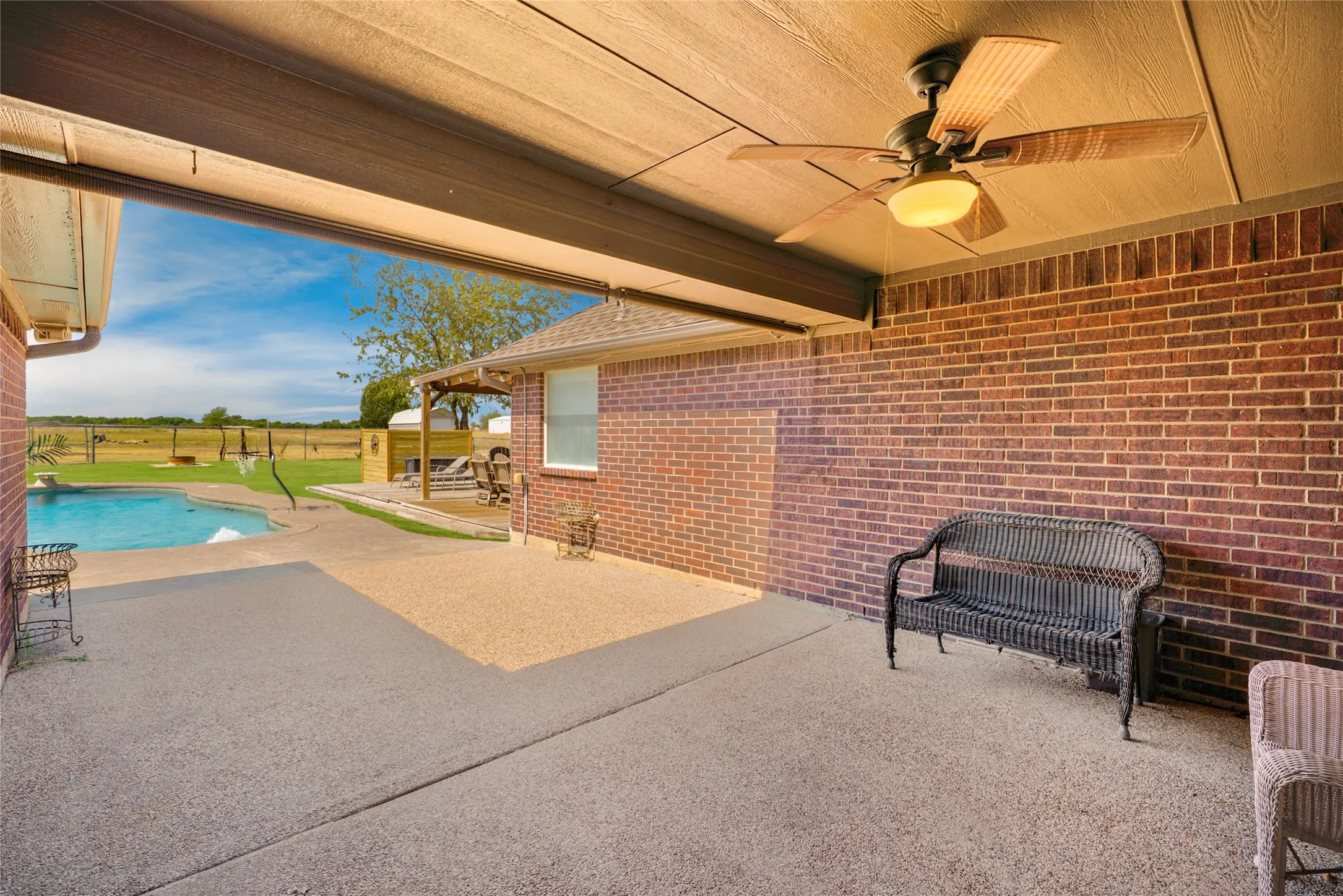 Covered patio with a ceiling fan, brick exterior, concrete patio, and a swimming pool
