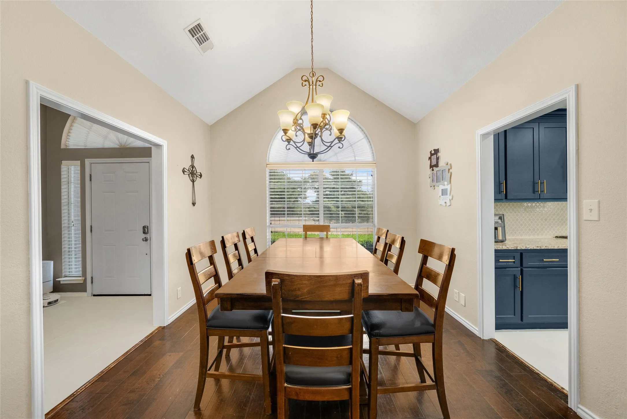 Vaulted ceiling with an ornate chandelier, wood-finish flooring, and a large arched window with horizontal blinds
