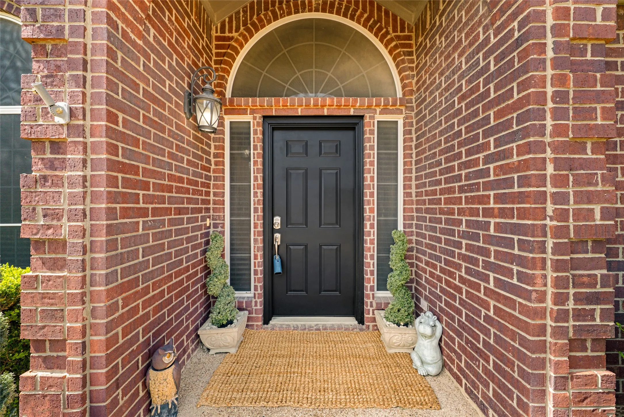 Brick exterior featuring an arched transom window, a paneled front door, sidelight windows, and a wall-mounted light fixture