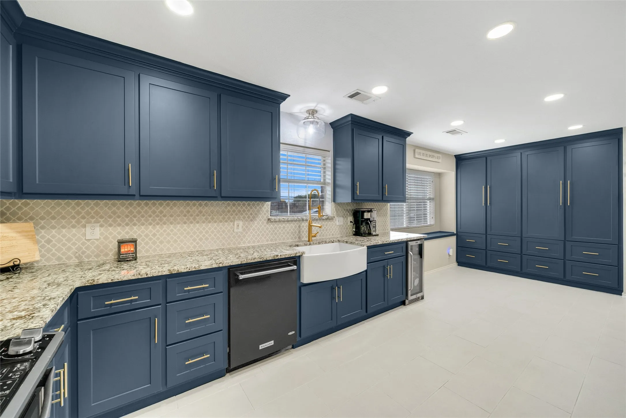 Well-appointed kitchen featuring extensive blue cabinetry, a white farmhouse sink, light-toned countertops, and a full-height tile backsplash