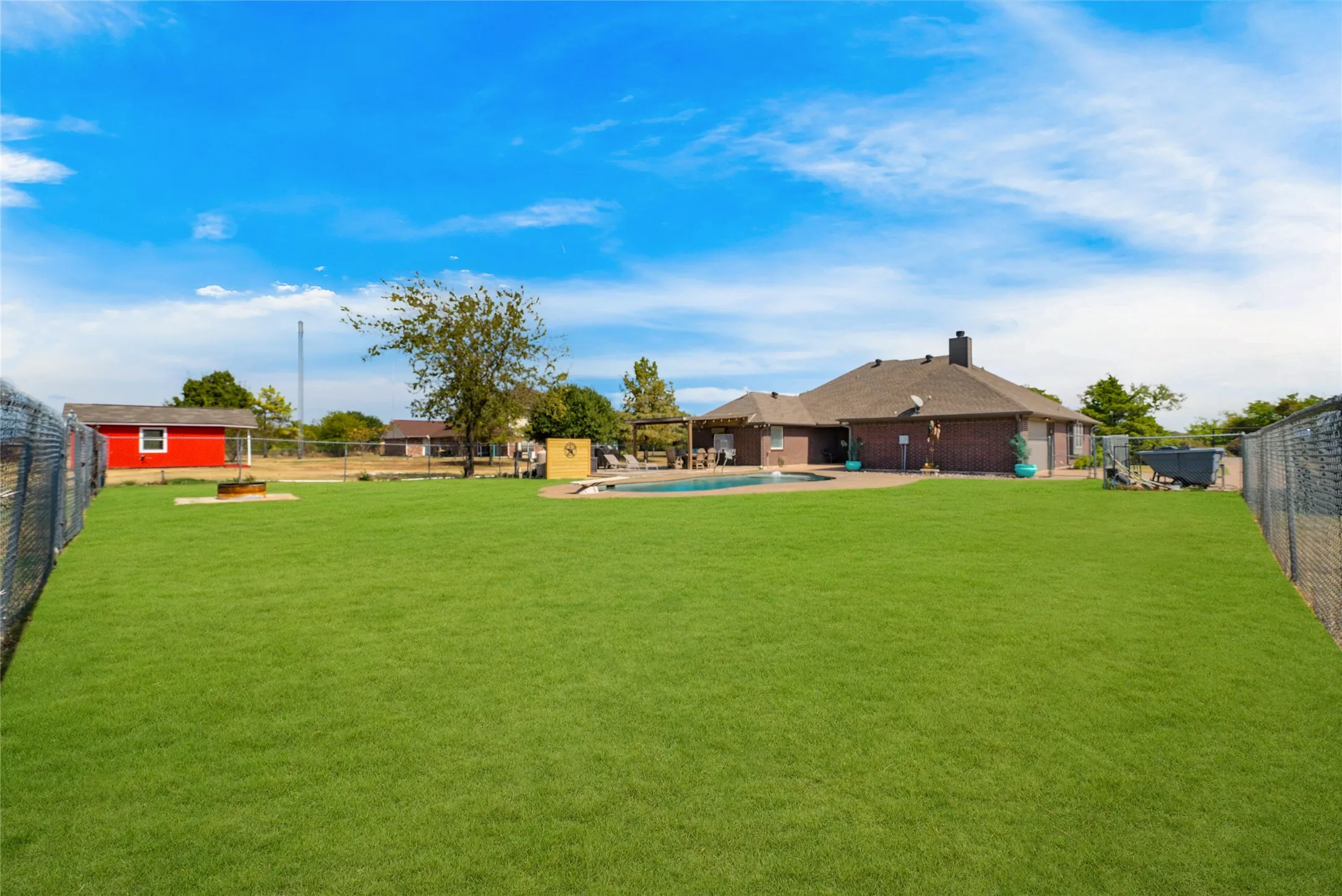 Expansive green lawn with chain link perimeter fencing, a brick exterior residence, and a swimming pool with surrounding hardscaping