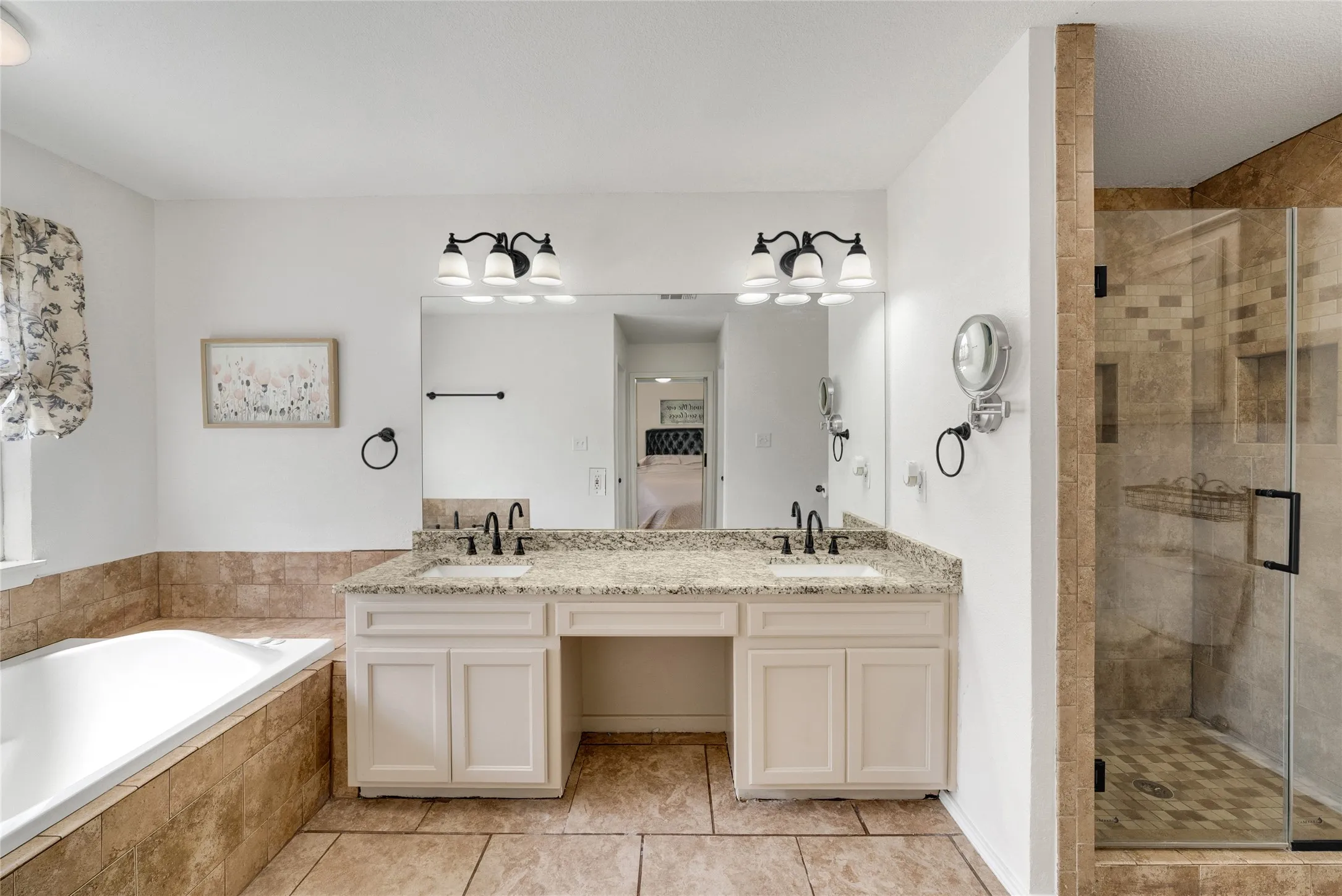 Dual vanity with integrated sinks, granite countertops, white cabinetry, a built-in tub, and a glass-enclosed shower with tiled walls