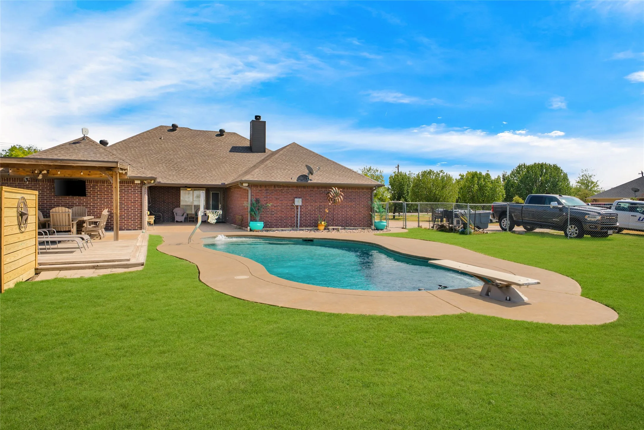Brick exterior residence featuring a swimming pool with diving board, a covered patio, and a grass lawn