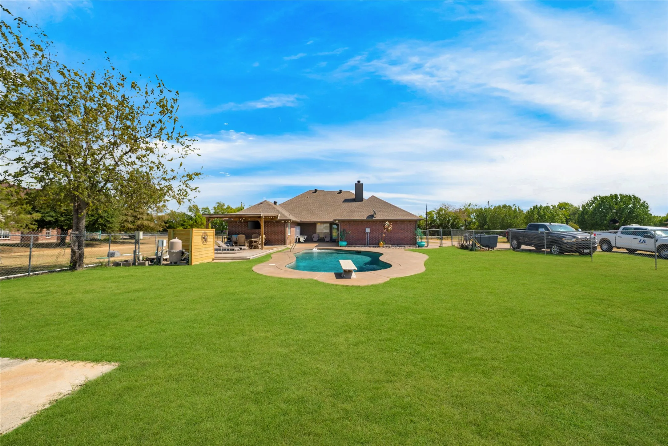 Expansive backyard featuring a large lawn, freeform swimming pool with diving board, and a covered patio area