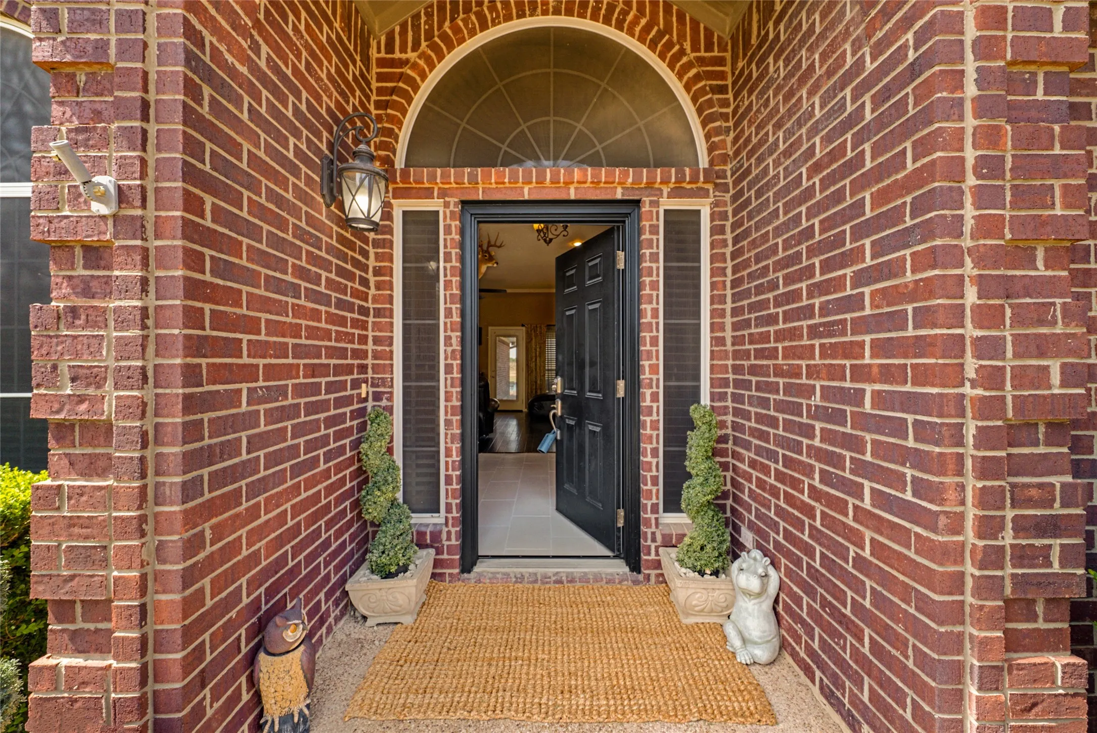 Red brick exterior with detailed brickwork, arched transom window, black paneled front door, and a built-in wall lantern