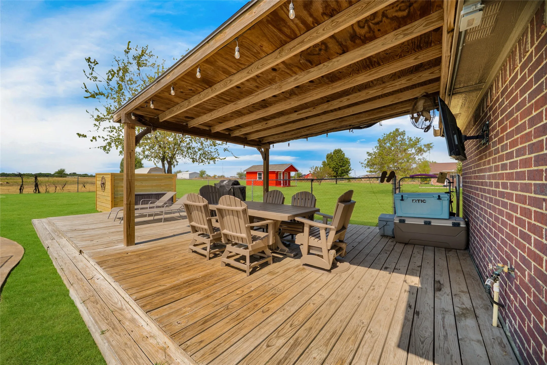 Expansive wood deck with a built-in pergola, brick exterior, and attached wall-mounted television