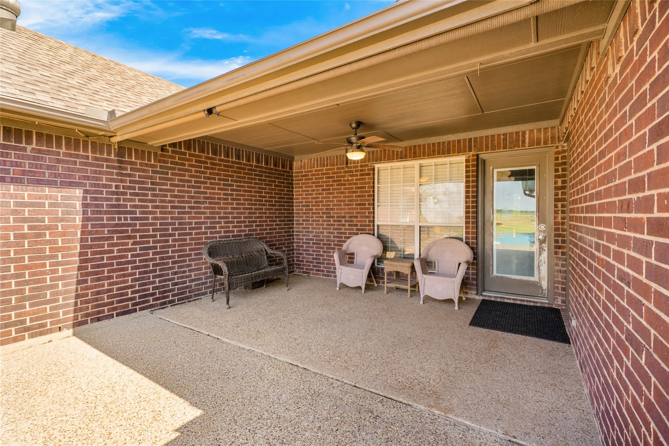 Covered patio with brick walls, exposed aggregate flooring, and a ceiling fan