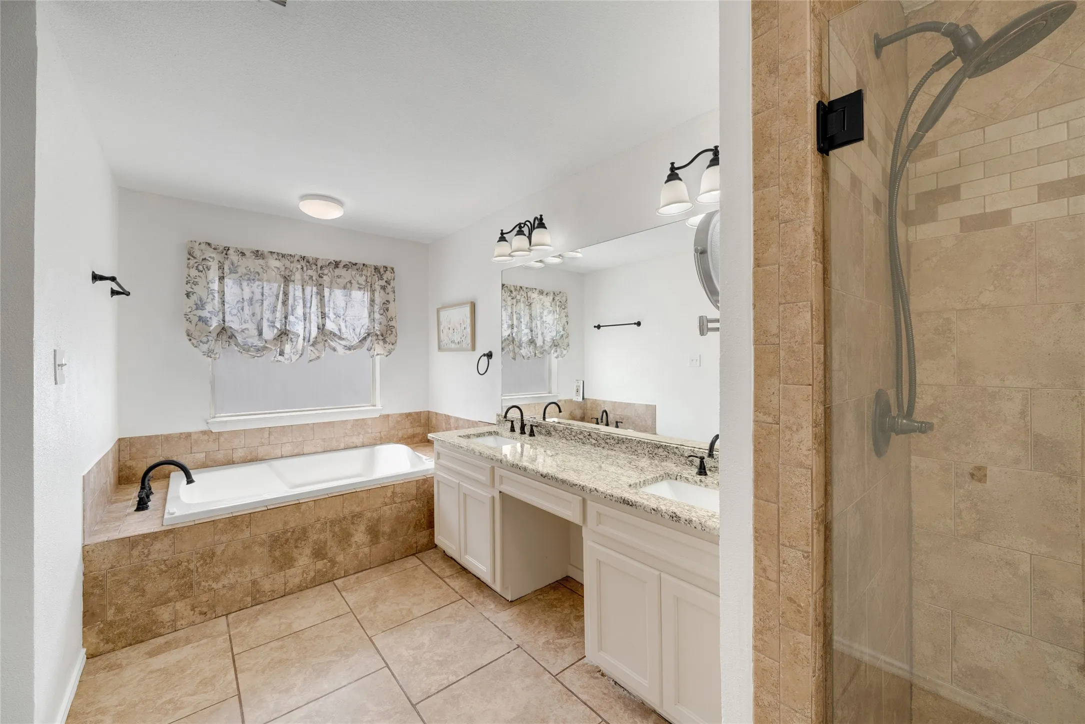 Spacious bathroom featuring a soaking tub, dual vanity with granite countertop, tiled flooring, and a walk-in shower with a tiled surround