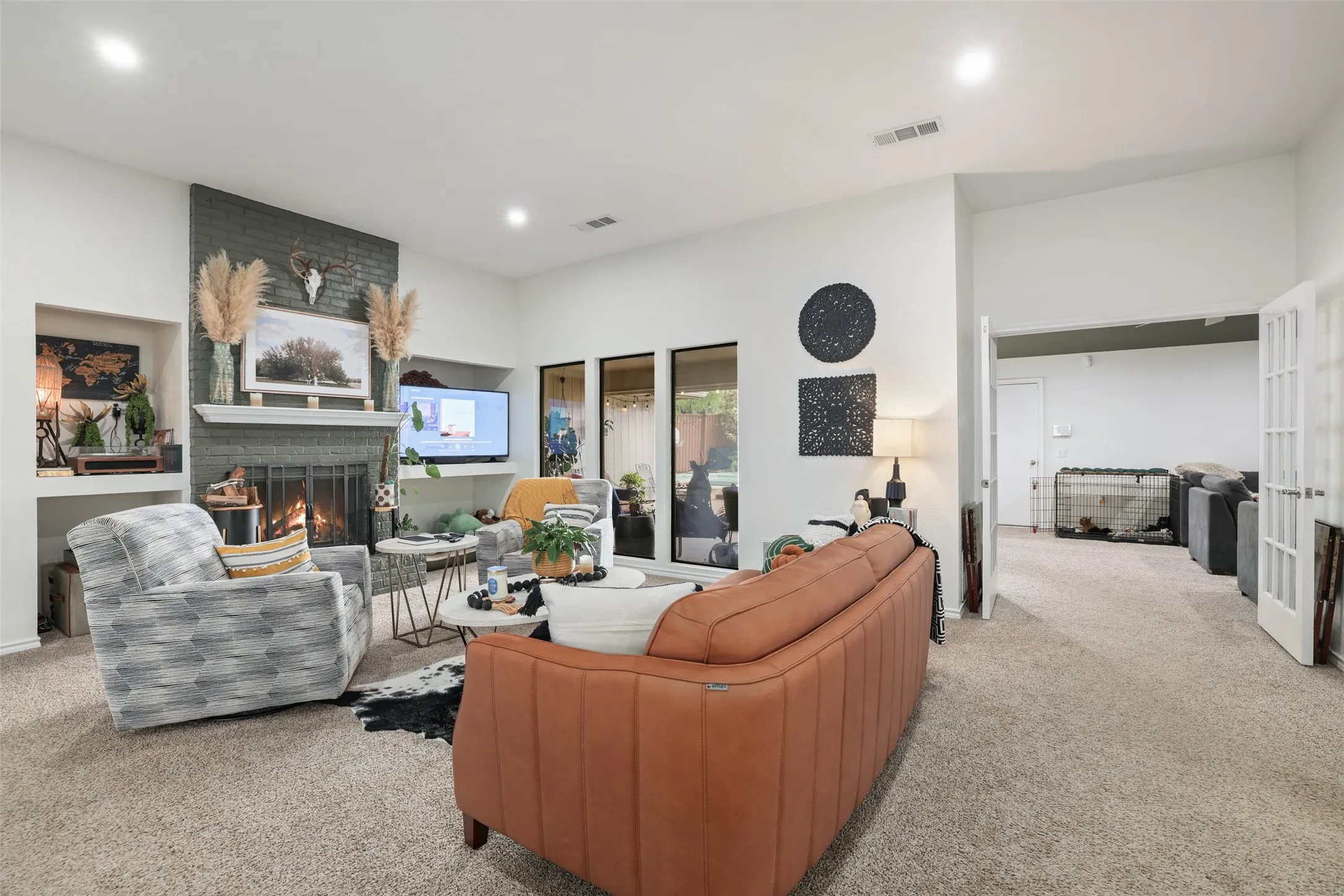 Vaulted ceiling living room featuring a fireplace with a brick surround, built-in shelving, recessed lighting, and access to an additional room through double French doors