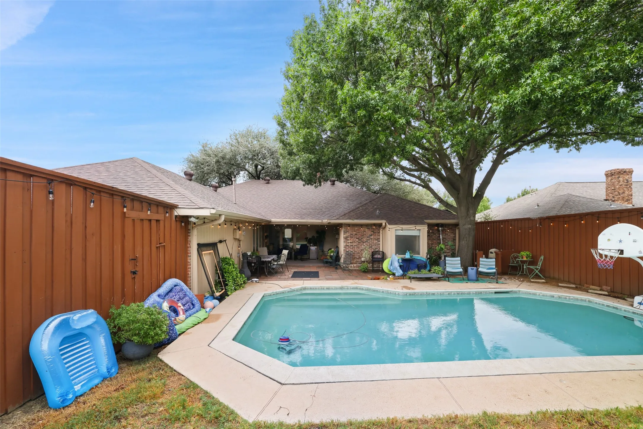 Private backyard oasis featuring a swimming pool with concrete surround, brick exterior, and a wood privacy fence