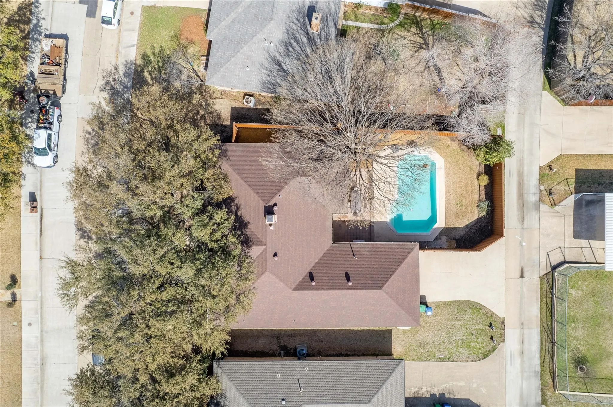 Contemporary brown shingle roof, expansive paved driveway, lush front yard landscaping, private swimming pool, and mature trees