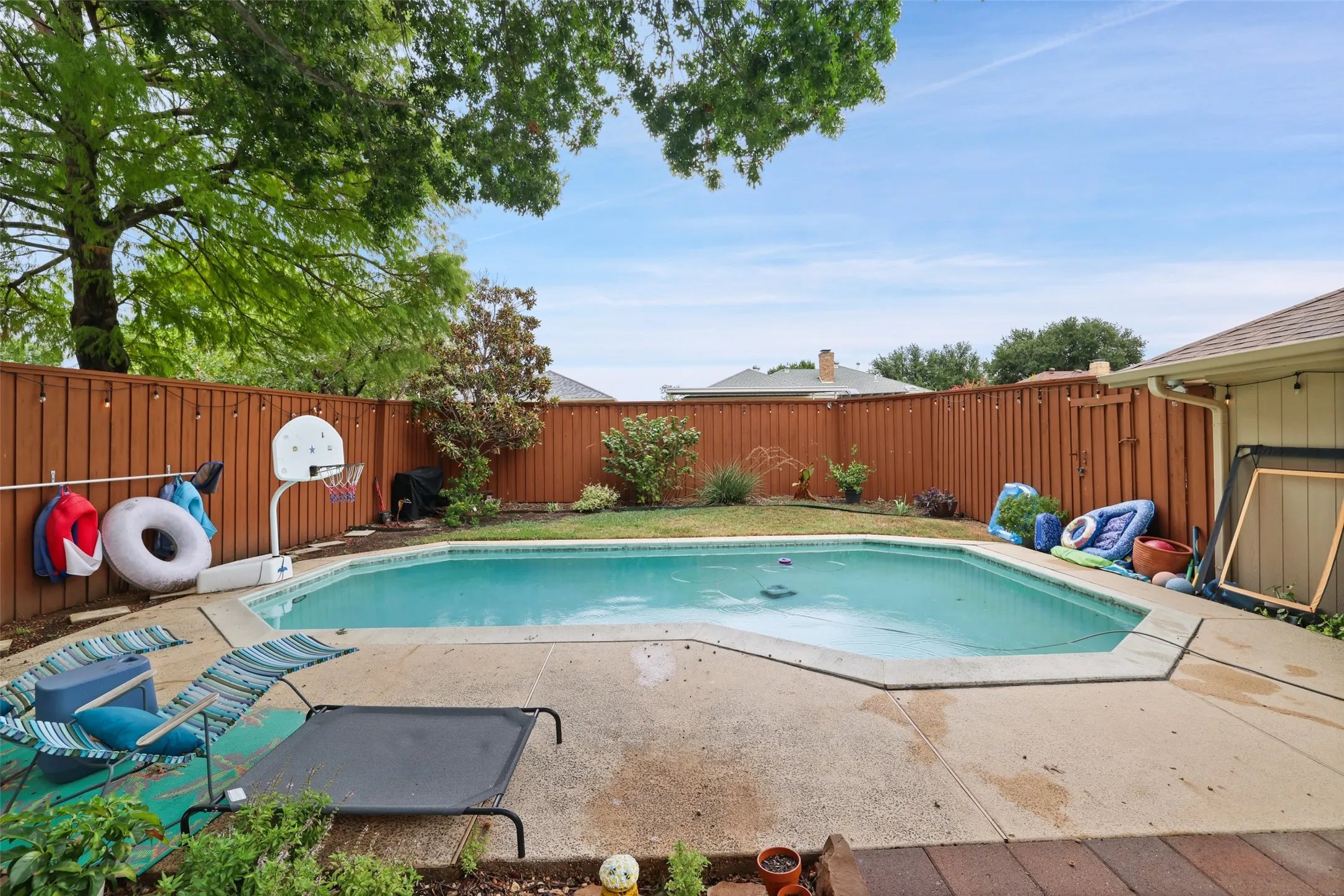 In-ground pool featuring a concrete surround, wood privacy fencing, and mature trees