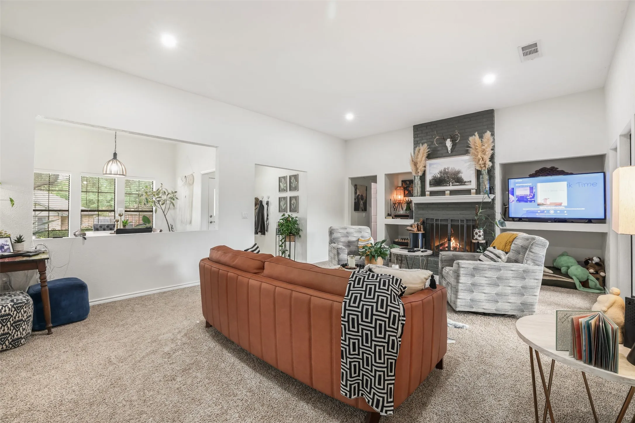 Living area with neutral carpeting, a gray brick-finish fireplace, and built-in shelving