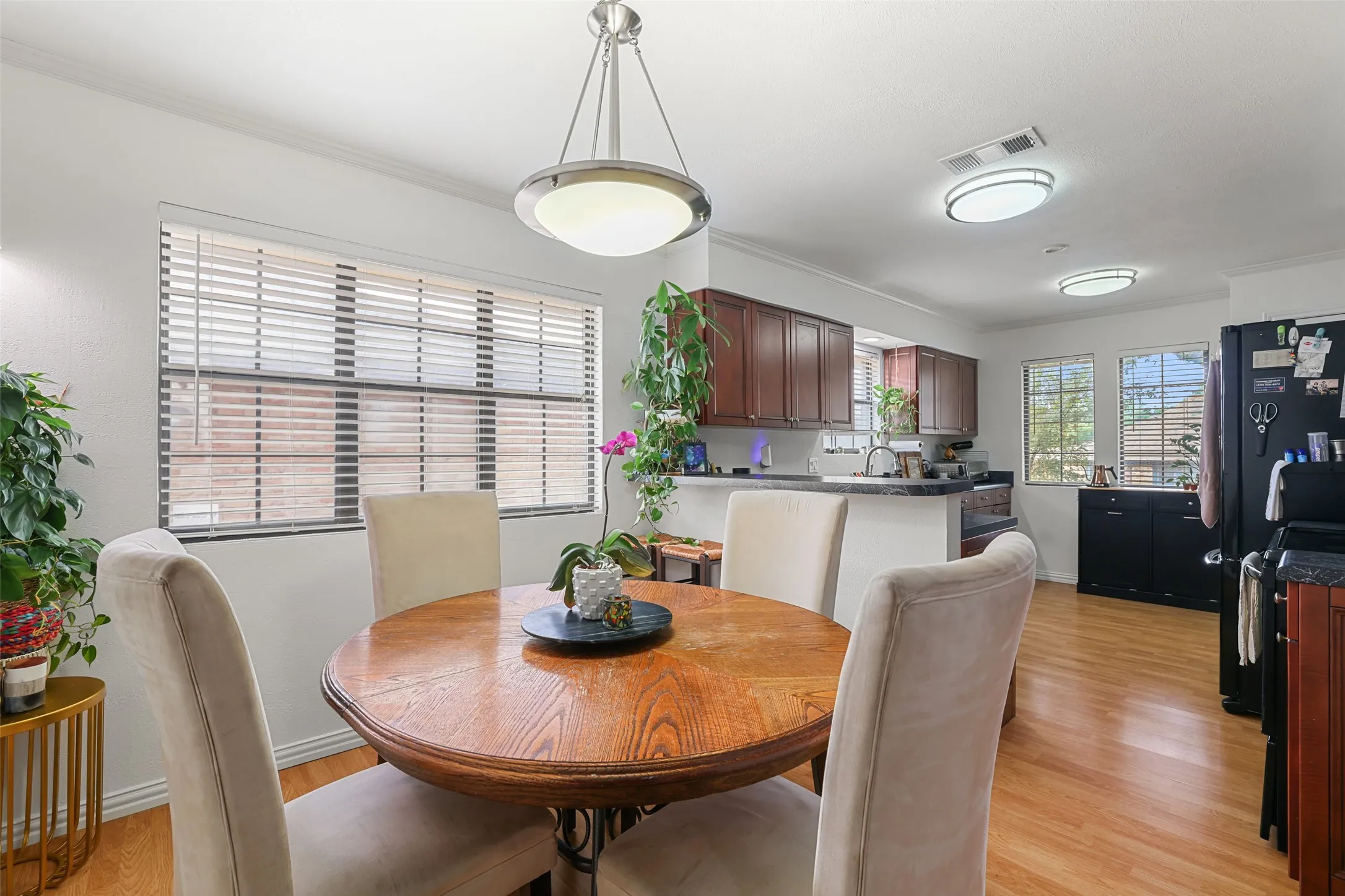 Dining area with wood-finish flooring, a contemporary pendant light fixture, and crown molding