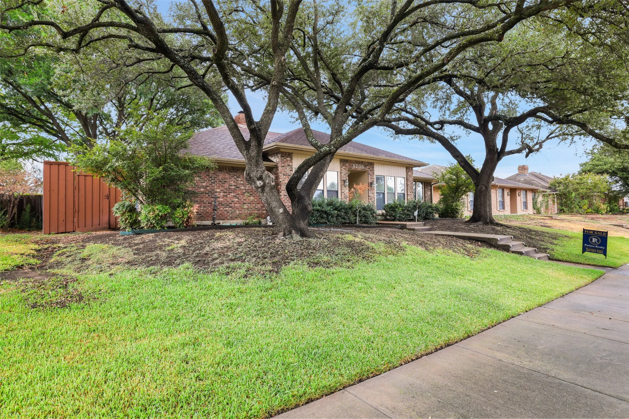 Brick exterior residence with a shingle roof, established landscaping, and a wood privacy fence