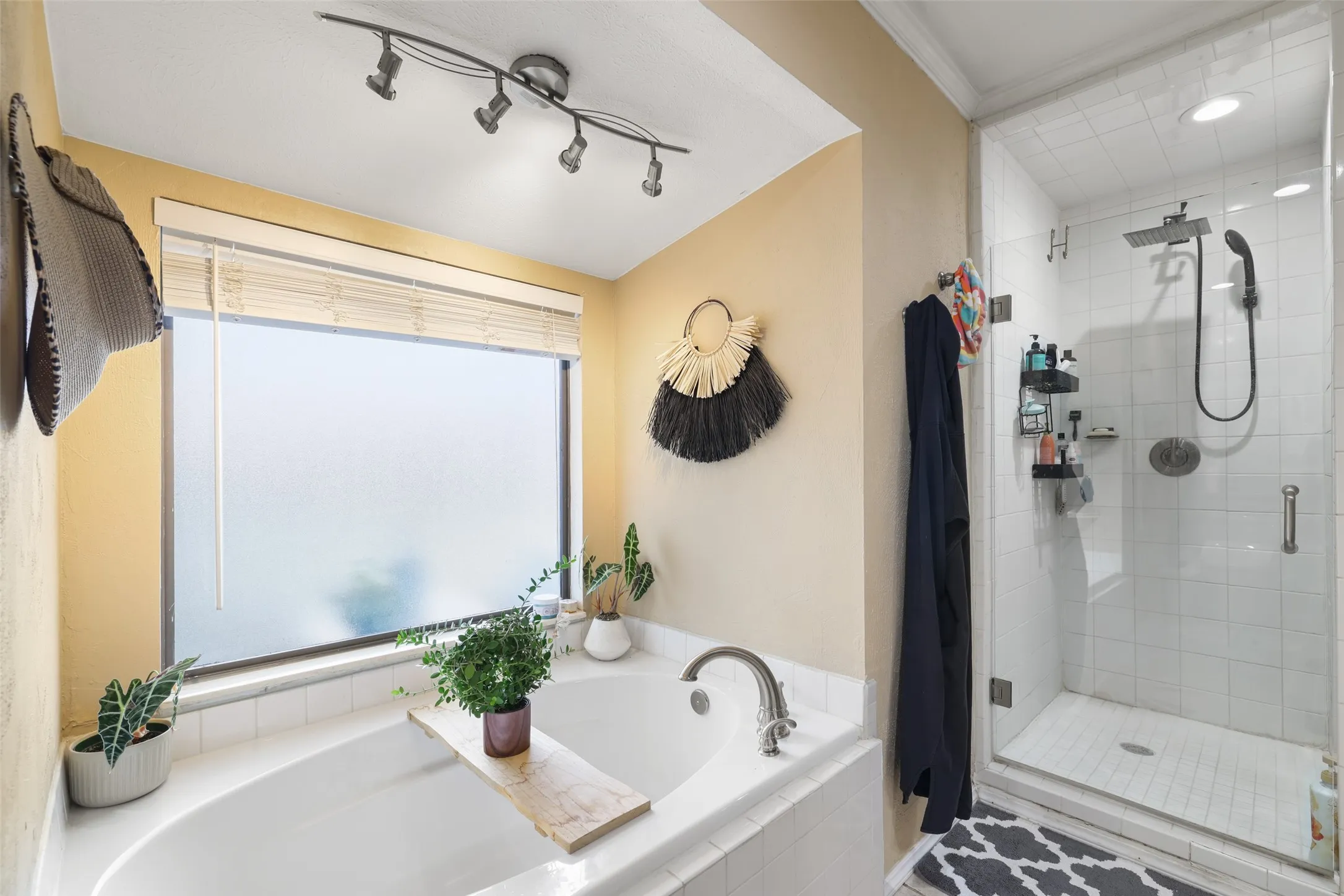 Soaking tub with tile surround, track lighting, and a glass-enclosed shower featuring a rainfall showerhead