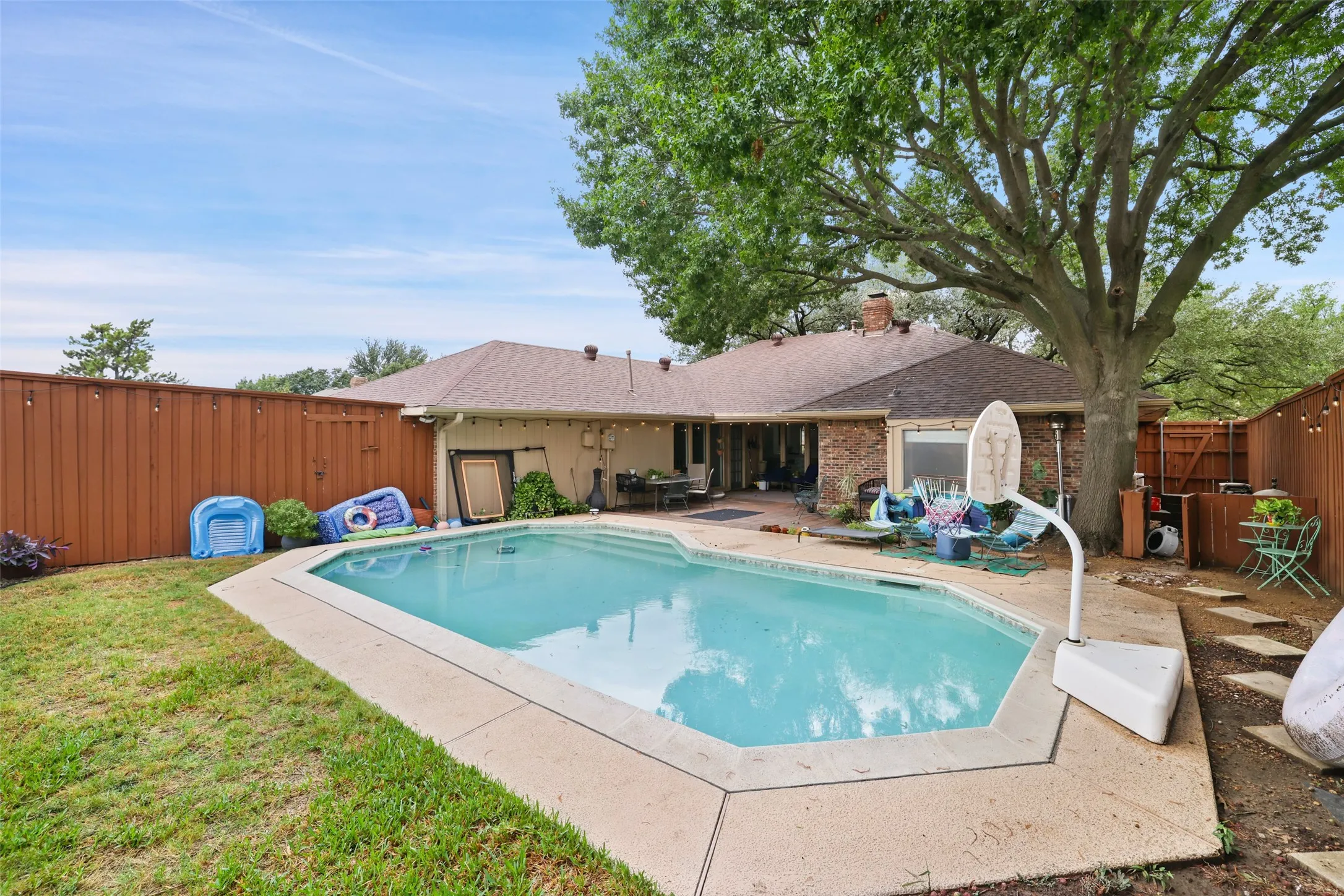 Backyard featuring an in-ground swimming pool with concrete decking, a large mature tree, and a wood privacy fence