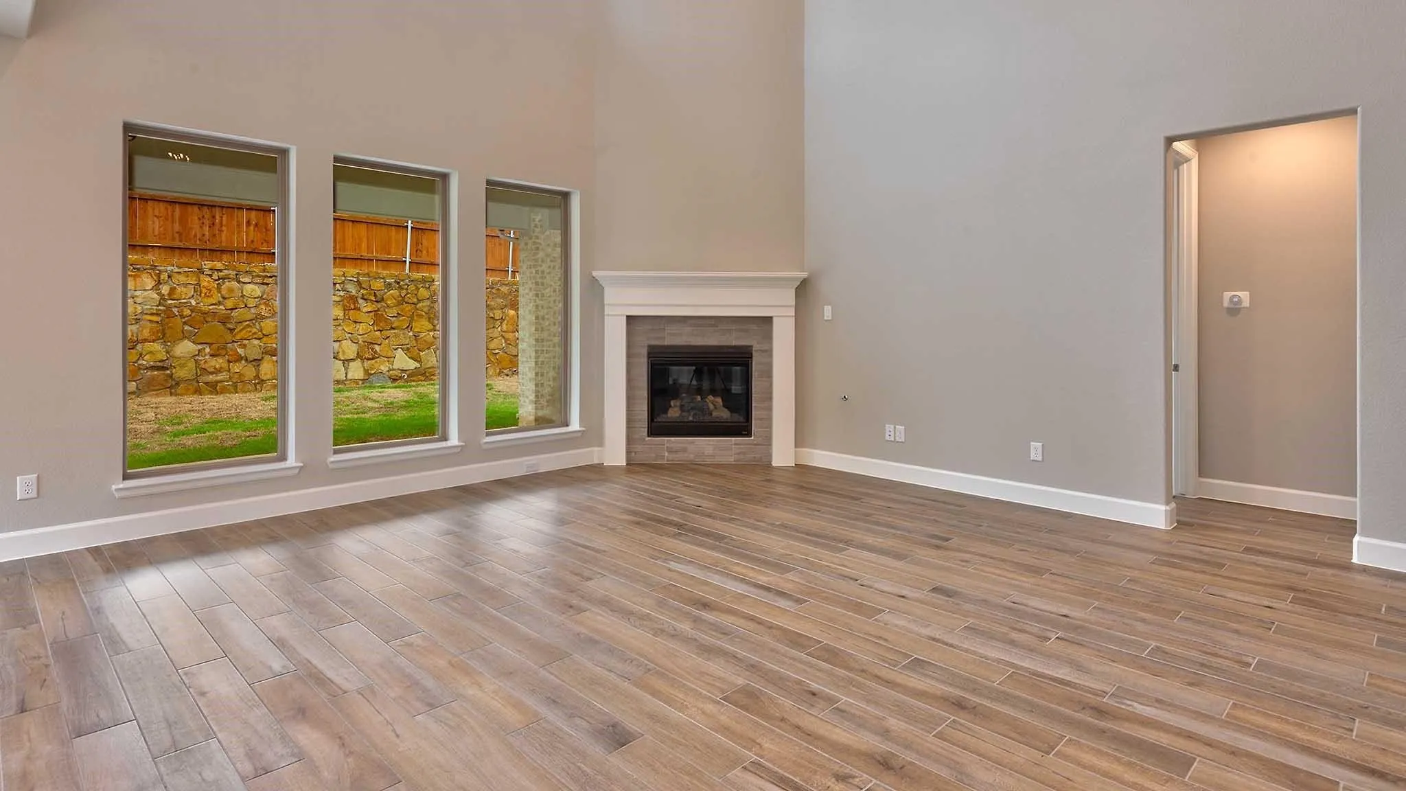 Vaulted ceilings with abundant natural light, wood-finish flooring, corner gas fireplace with tile surround and mantel, and recessed entry