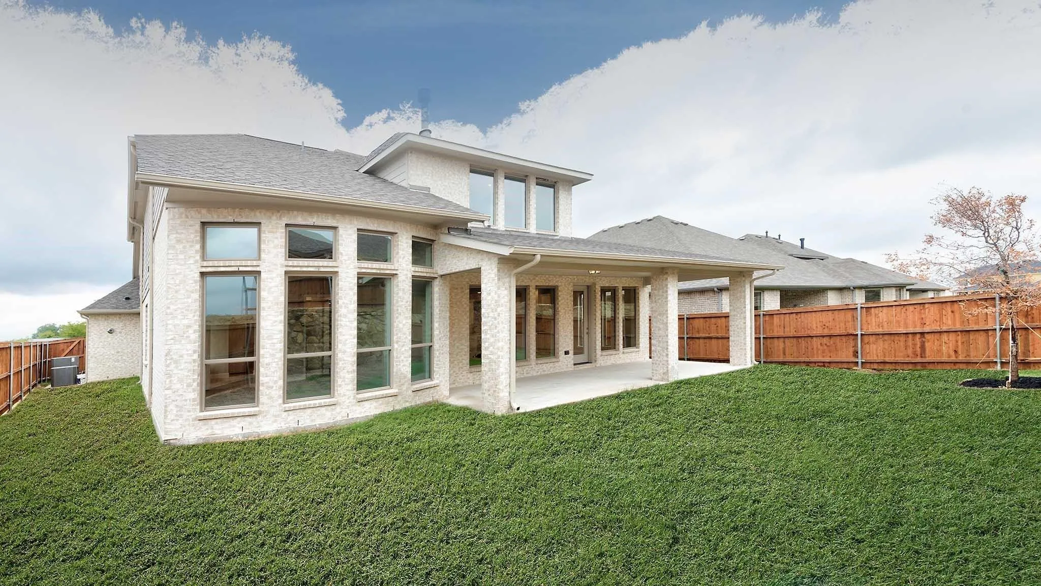 Expansive backyard with a manicured lawn, full privacy fencing, covered patio, and large windows