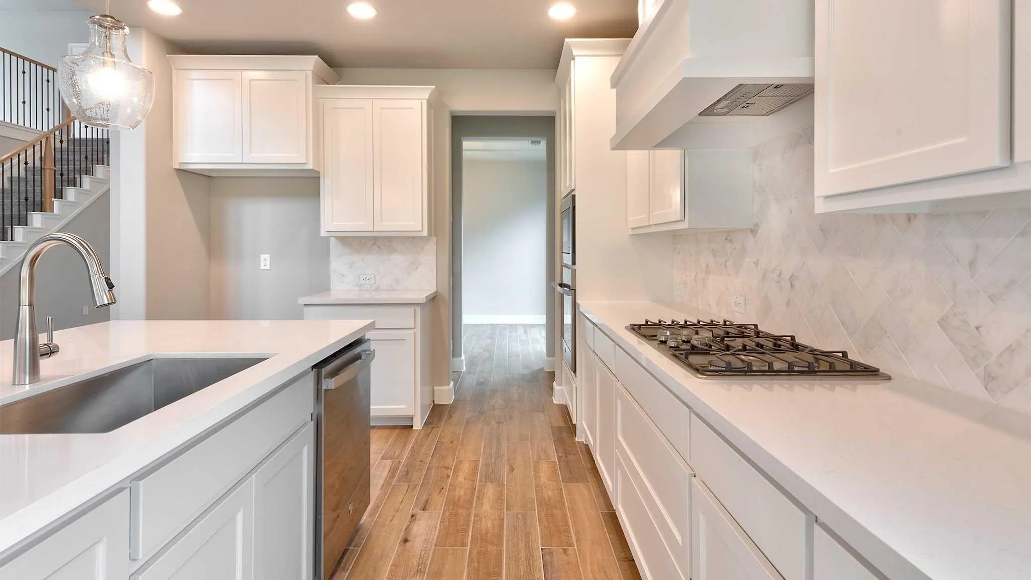 Kitchen featuring white shaker cabinetry, light-toned countertops, a stainless steel sink, wood-finish flooring, and a gas cooktop with a built-in ventilation hood
