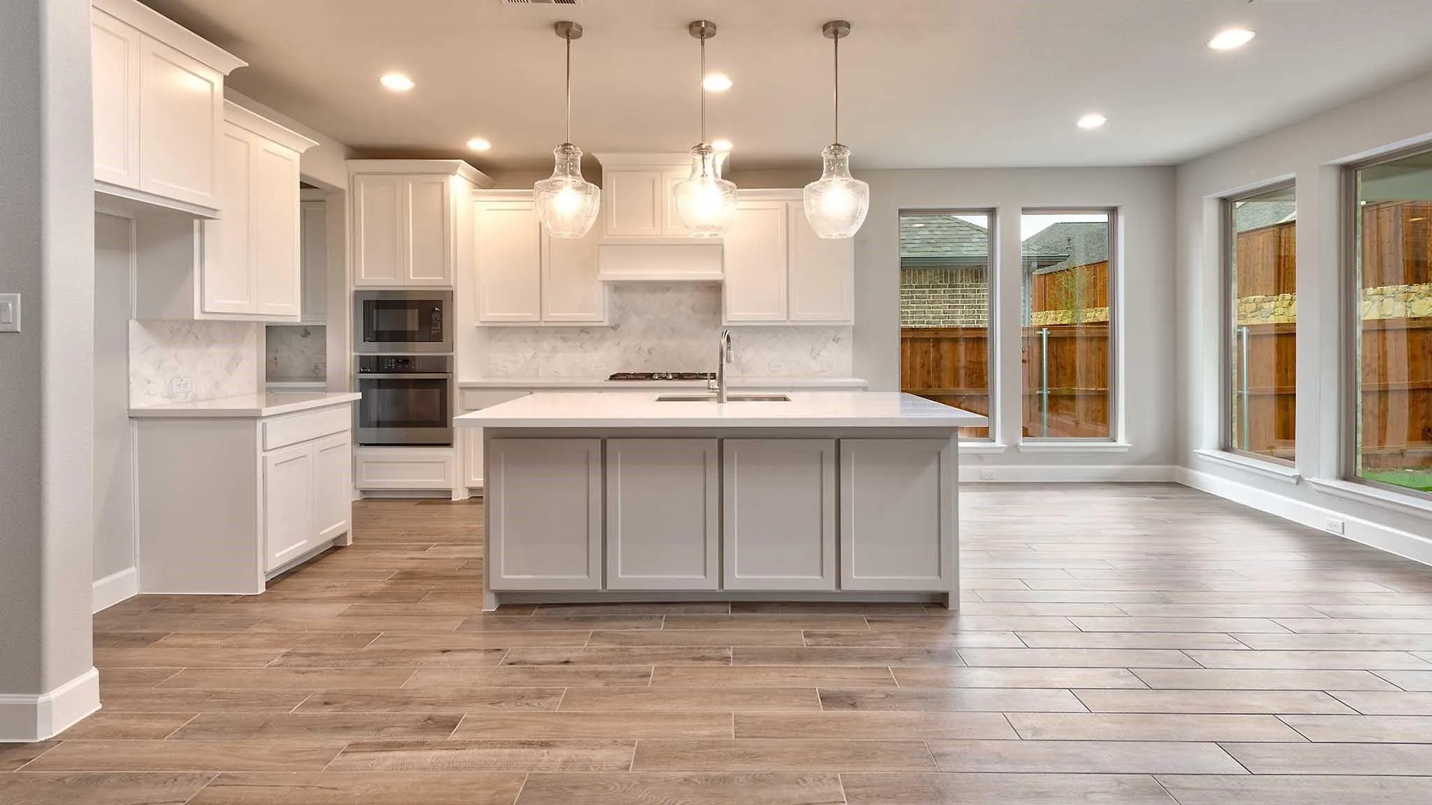 Open-concept kitchen with white shaker cabinetry, an expansive central island, stainless steel double ovens, and wood-finish flooring
