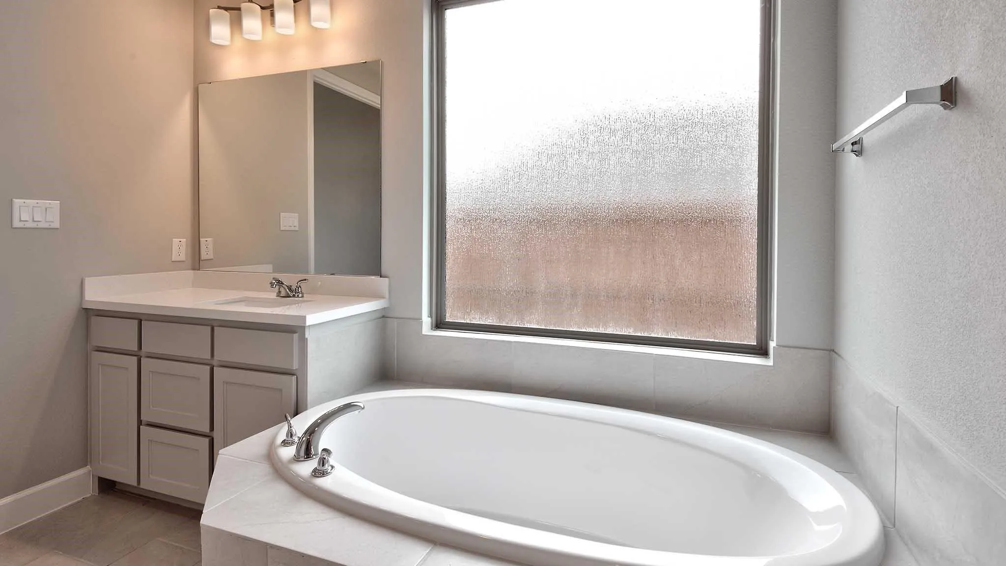 Built-in bathtub with deck-mounted fixtures, vanity with undermount sink, countertop, mirror, and wall-mounted light fixture