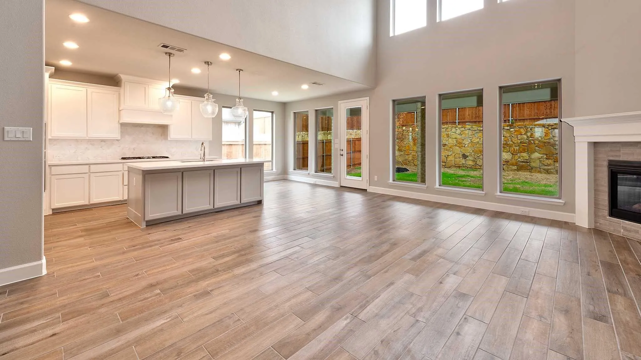 Open-concept living space featuring wood-finish flooring, a contemporary kitchen island with pendant lighting, a tile-surround fireplace, and expansive windows